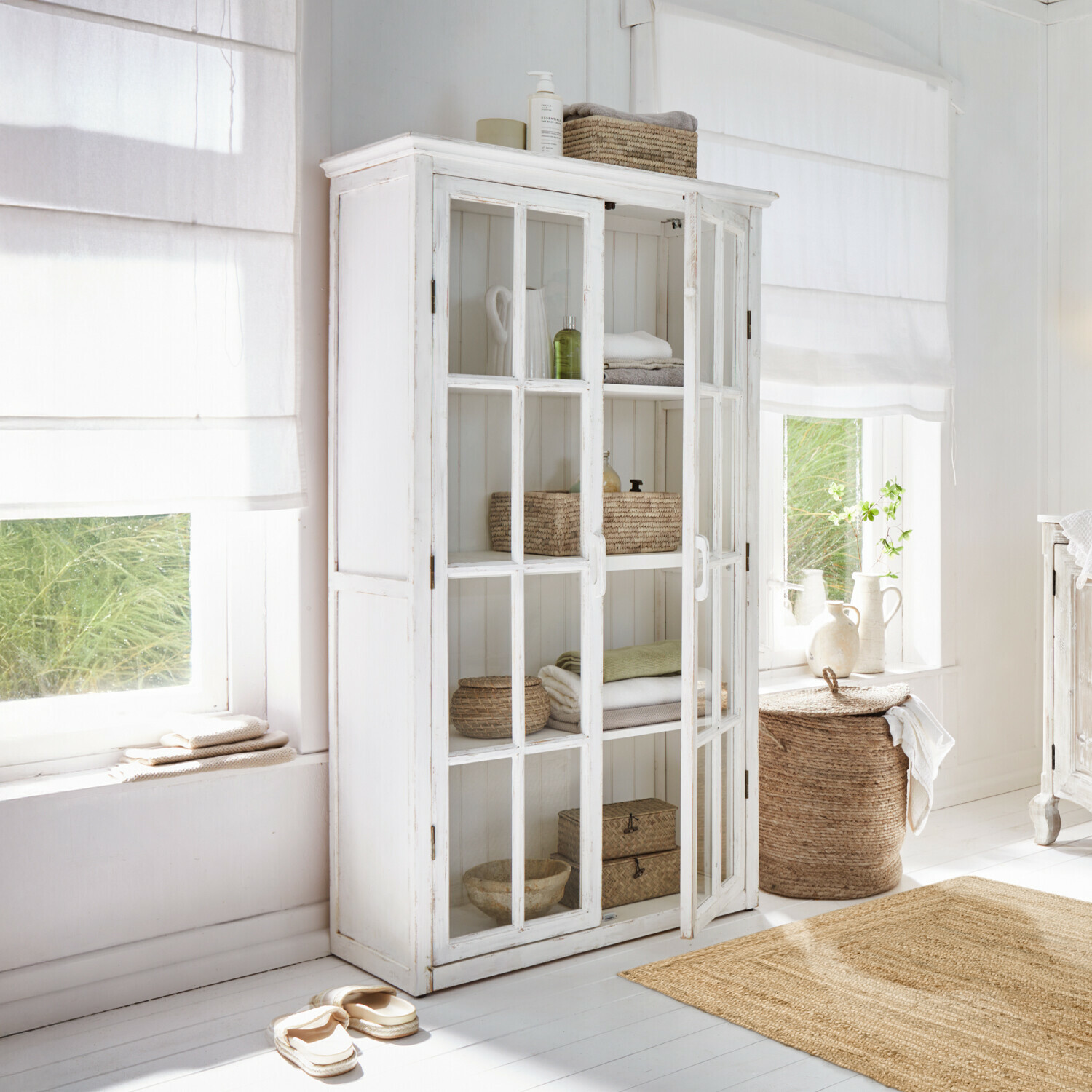 Vitrine Keanu Armoire blanche en bois avec portes vitrées dans une pièce lumineuse décorée d'éléments naturels et textiles