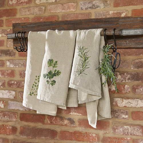 Torchons en lin couleur naturelle avec motifs d'herbes suspendus sur un porte-serviettes en bois devant un mur en briques