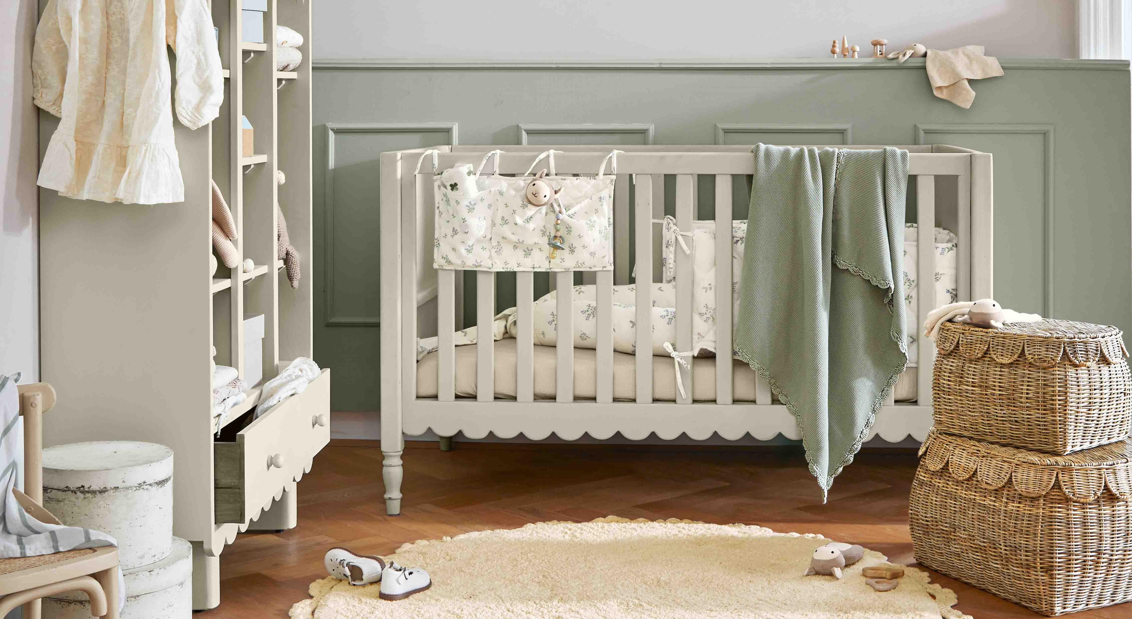 Grijs houten babybed met groene deken en rieten manden in een gezellige kinderkamer