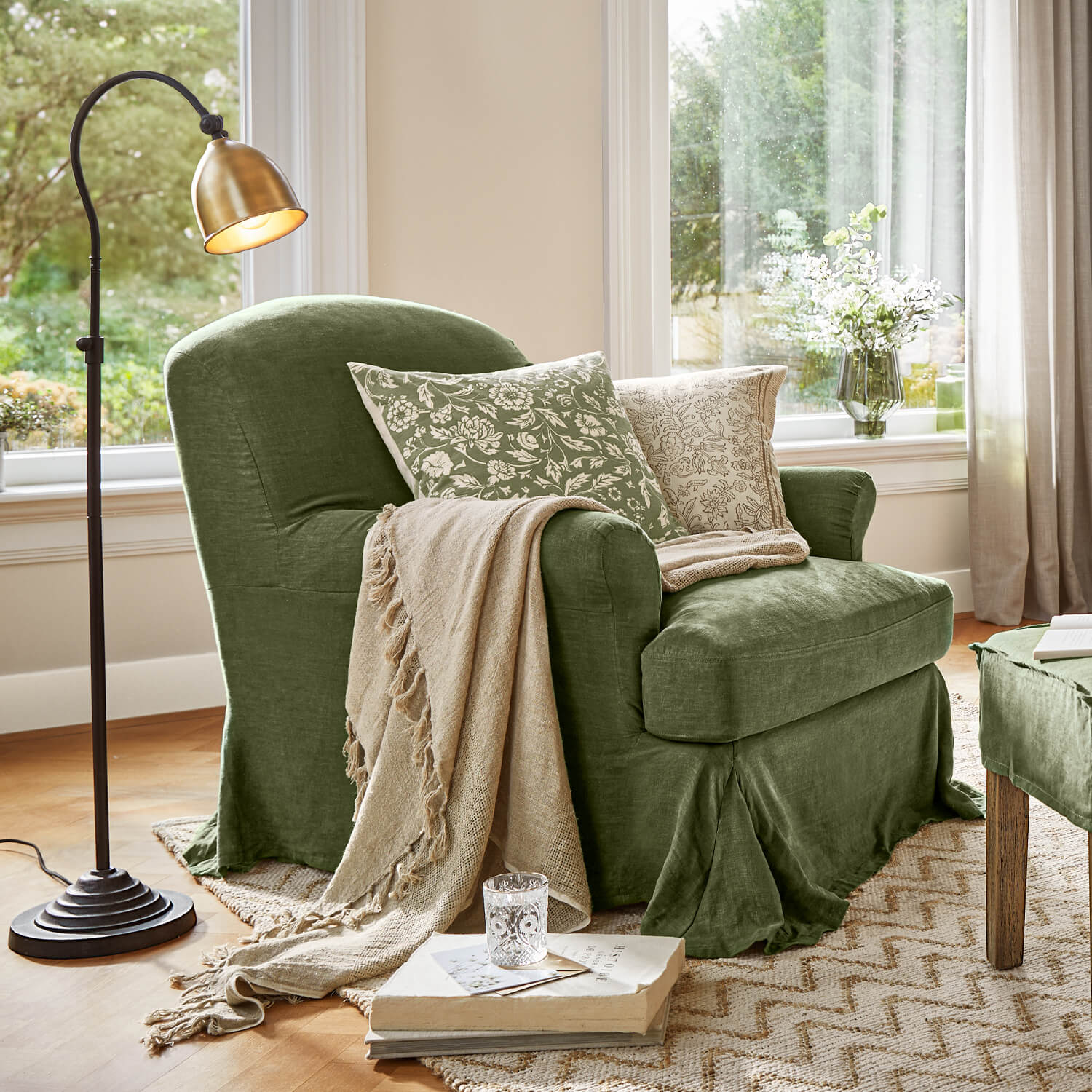 Groene stoffen fauteuil met beige deken en bloemenkussens in lichte woonkamer