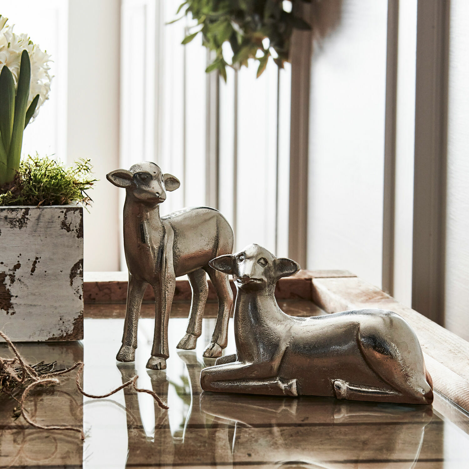 Twee zilverkleurige metalen hertenfiguren op glazen tafel, rustieke interieurdecoratie