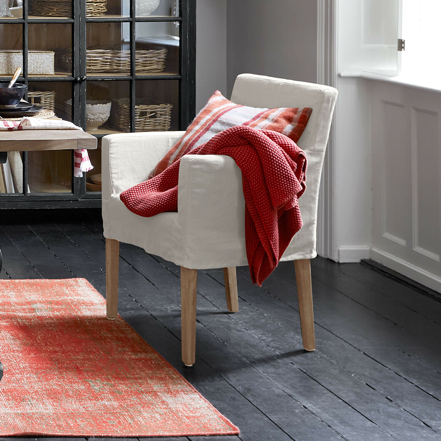 Stoel Longhill Beige fauteuil met houten poten, rode deken en geruit kussen in een gezellige kamer