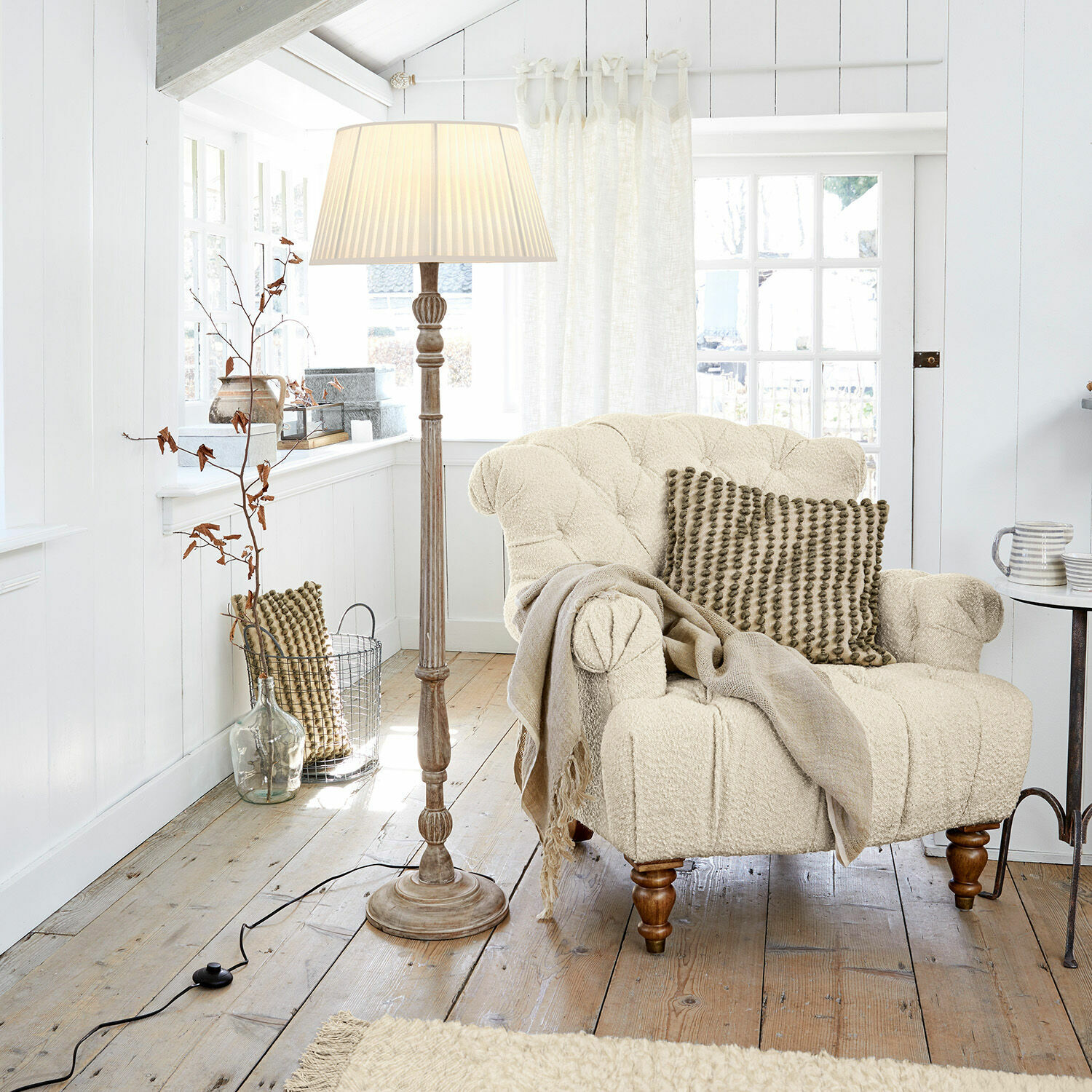 Lampadaire Morten Fauteuil beige en tissu bouclé avec coussin et lampe sur pied dans un salon lumineux en bois