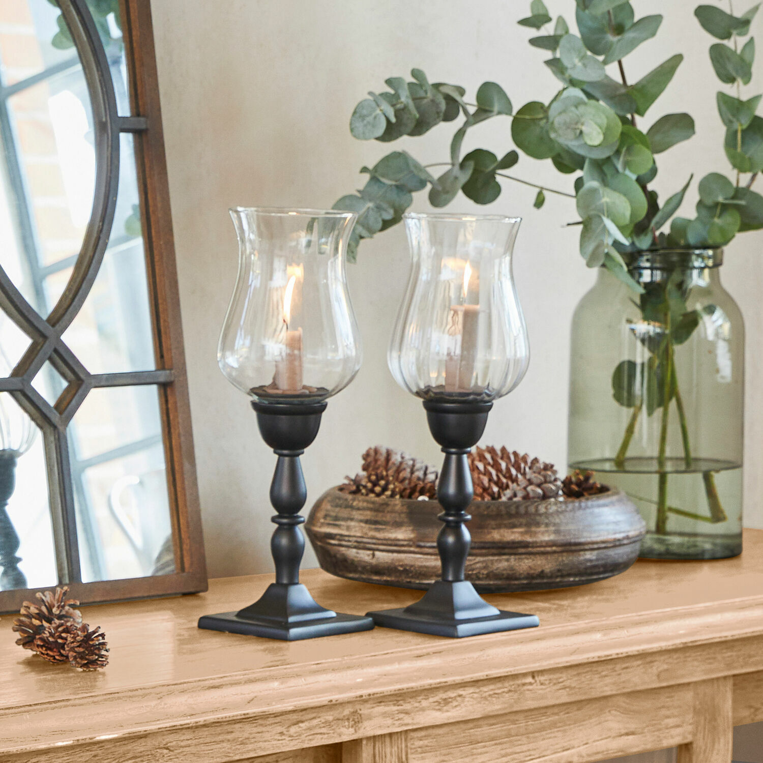 Paire de bougeoirs noirs avec verre transparent sur table en bois décorée de pommes de pin