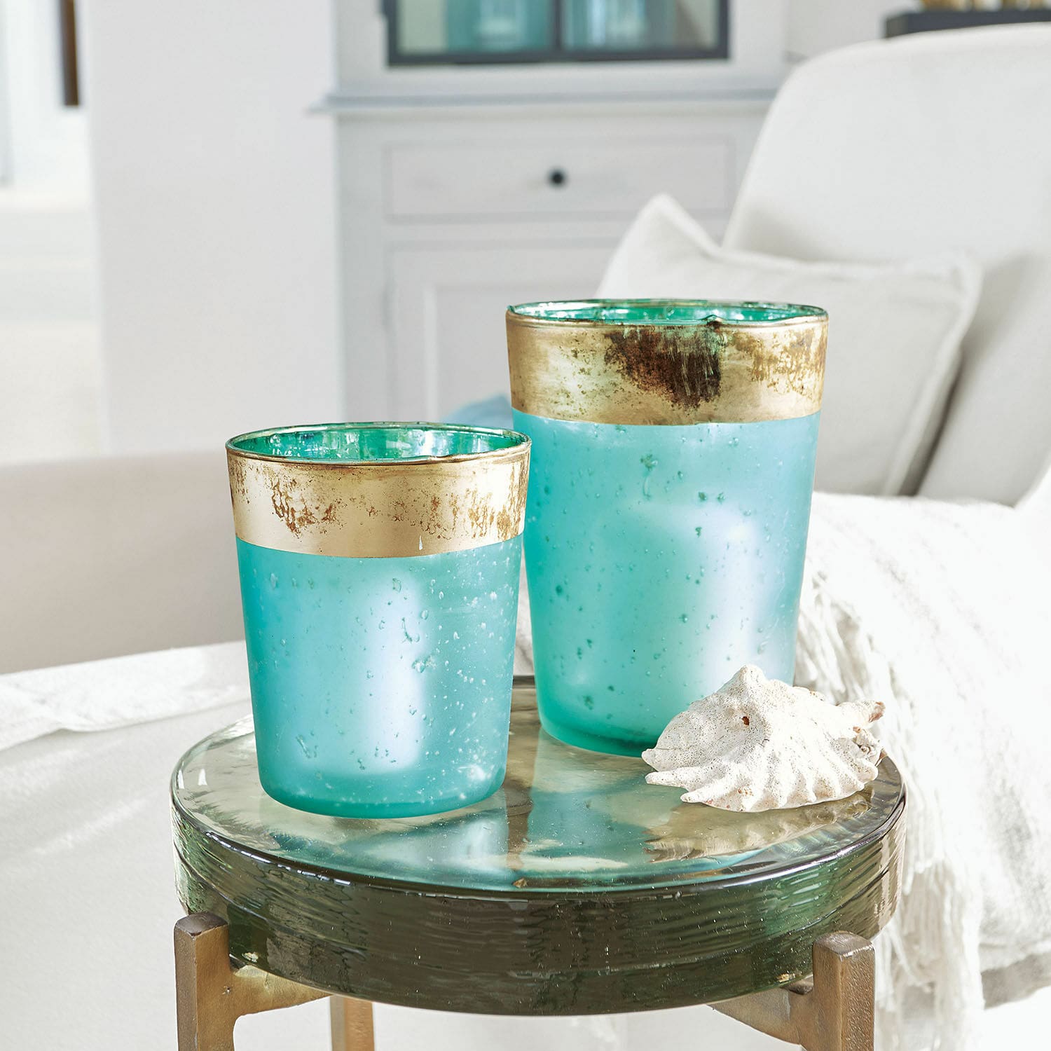 Lot de 2 photophores Ewena Deux photophores en verre turquoise avec bordure dorée sur une table en verre décorative