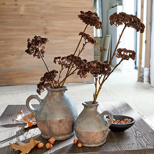 Twee grijsbruine keramische kannen met gedroogde bloemen op een houten tafel met hazelnoten