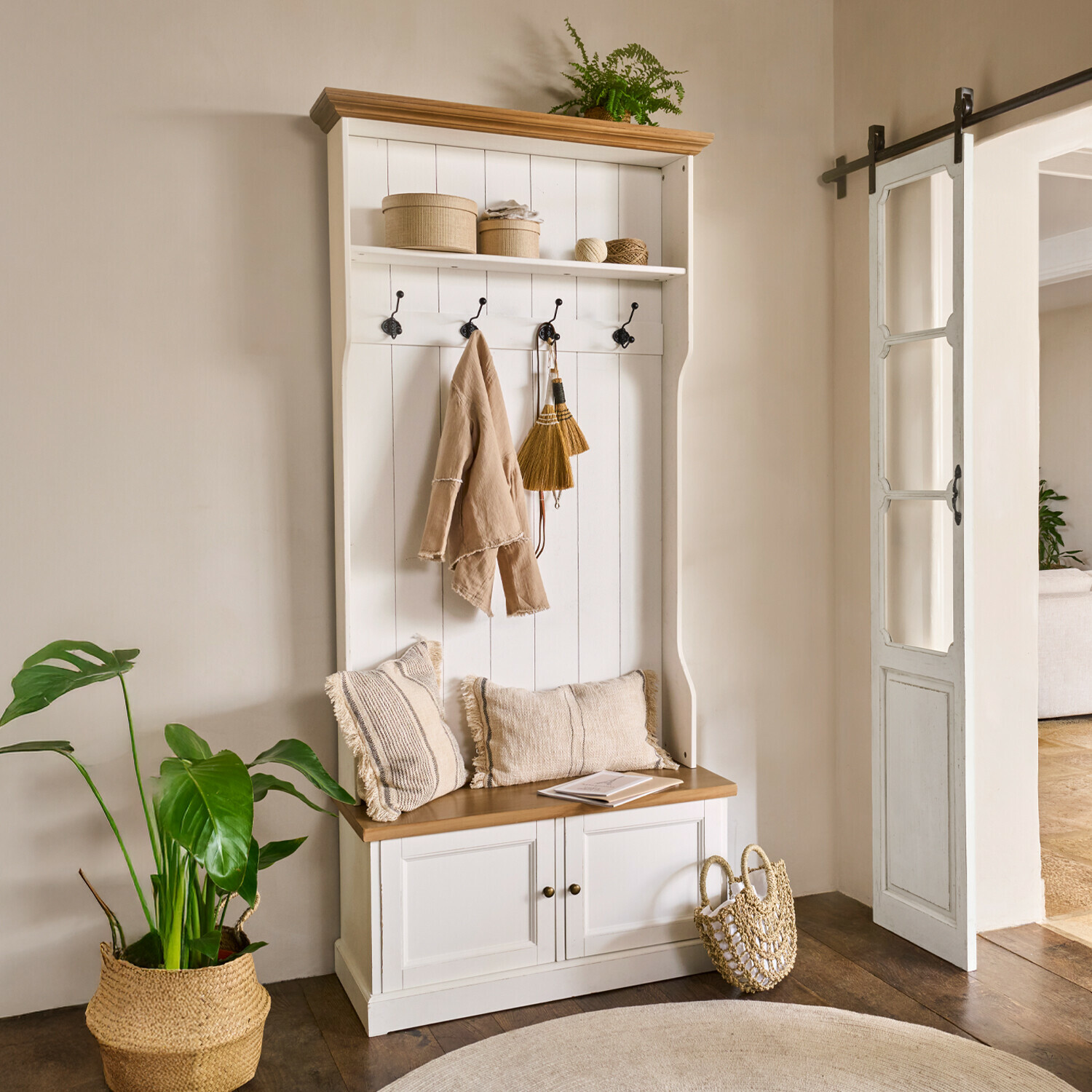 Witte houten kast met haken en plank, natuurlijke accessoires en beige kussens in de hal