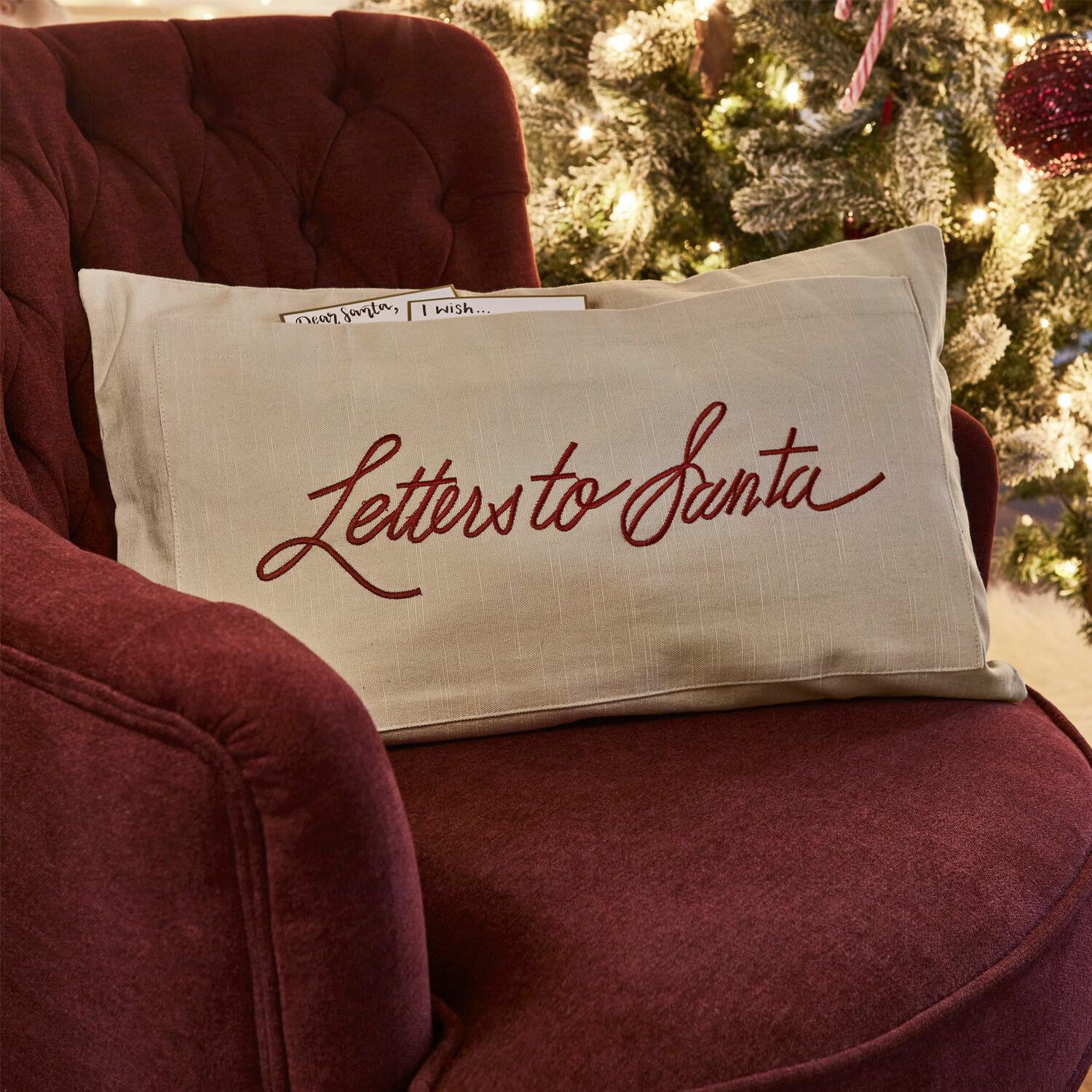 Beige linnen kussen met rode tekst Letters to Santa op bordeauxrode stoel bij kerstboom
