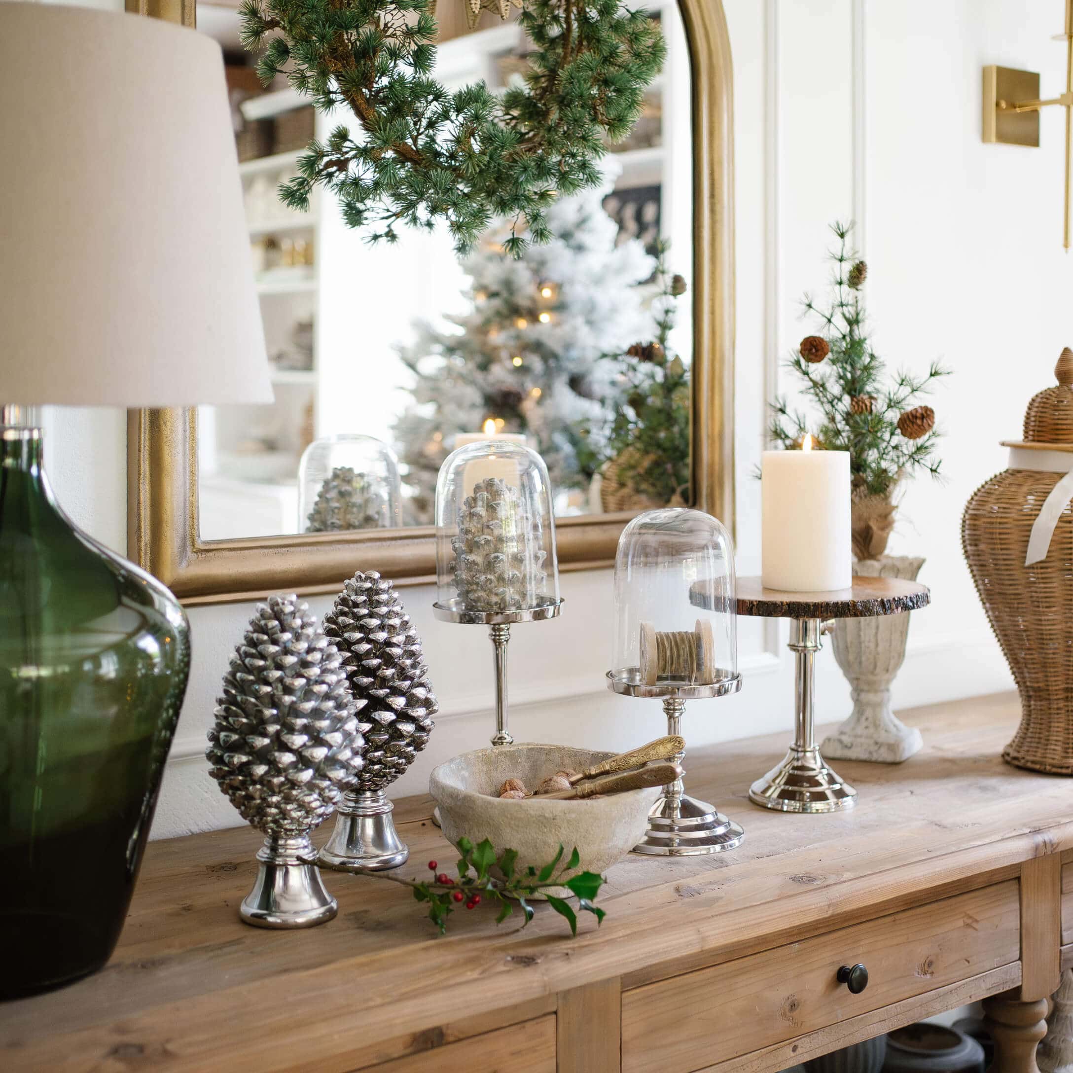 Décorations pommes de pin argentées et bougie sur table en bois dans un intérieur rustique avec accents verts
