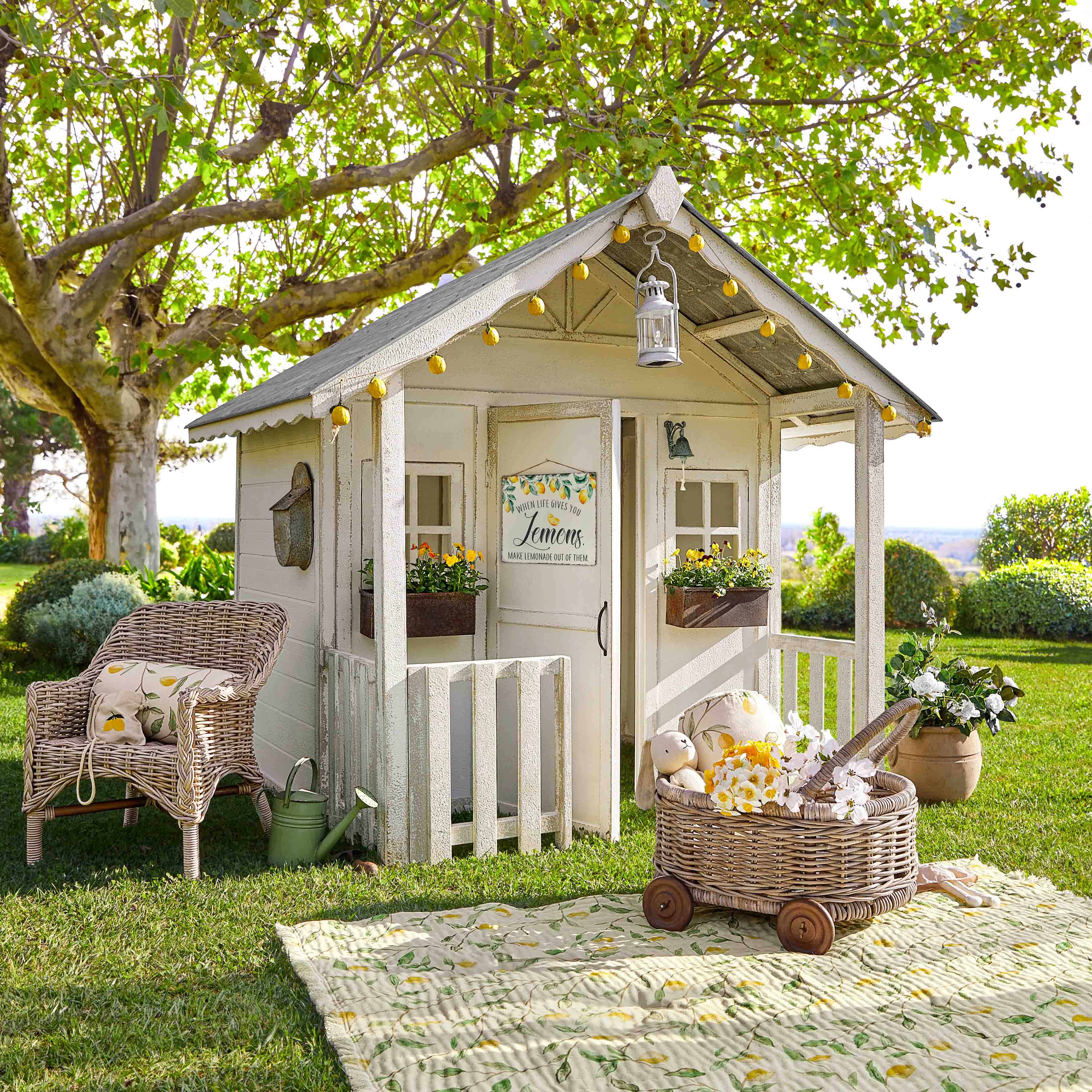 Maisonnette de jardin blanche en bois avec décorations citron et fauteuil en osier sur pelouse verte