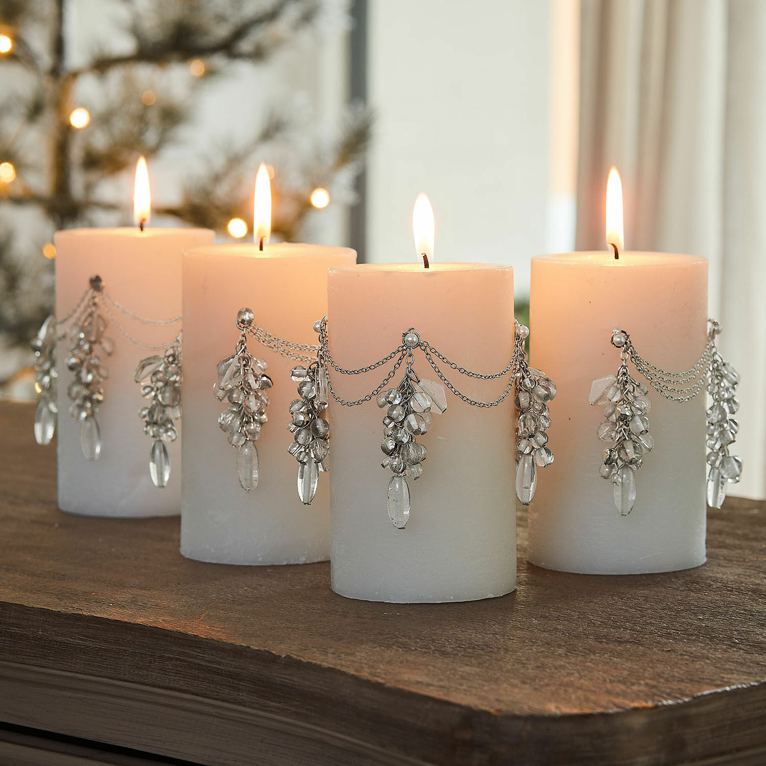 Lot de 4 pin’s décoratifs Gisolée Ensemble de quatre bougies blanches décorées de chaînes argentées et pendentifs en cristal sur une table en bois