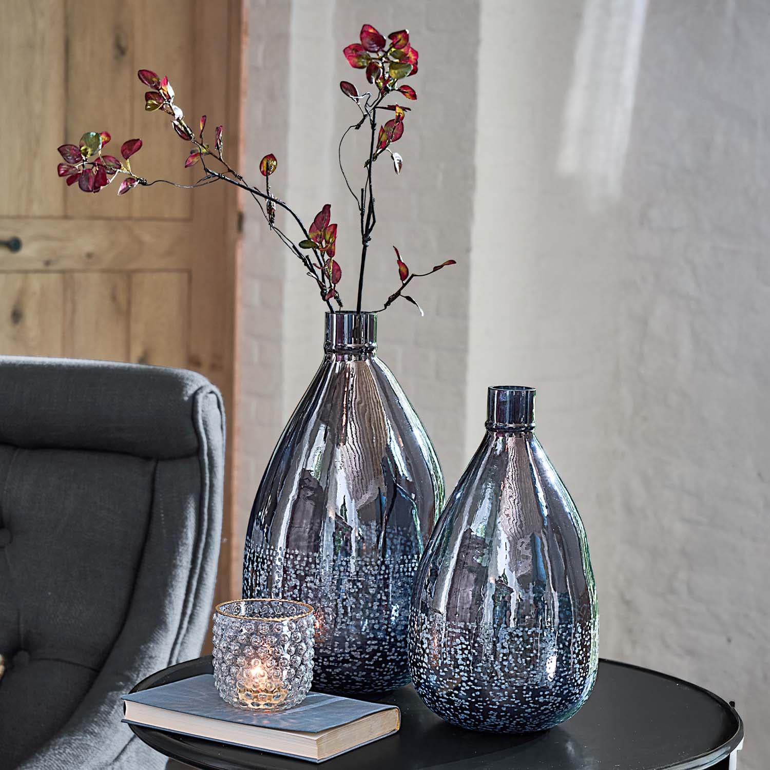 Twee decoratieve rookglas vazen met bubbels op een zwarte tafel naast een kaarsenhouder en boek