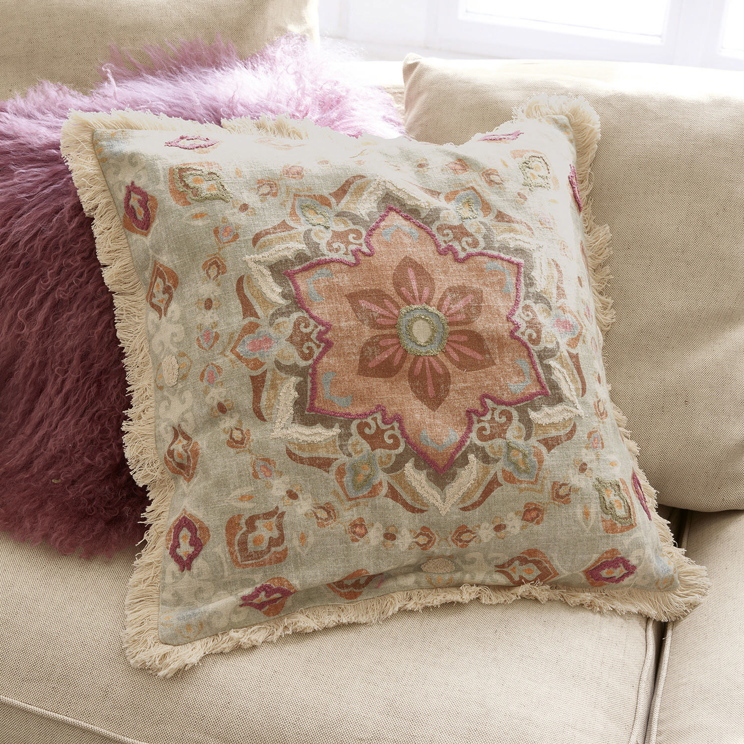Coussin décoratif en coton avec franges et motif pastel sur canapé beige