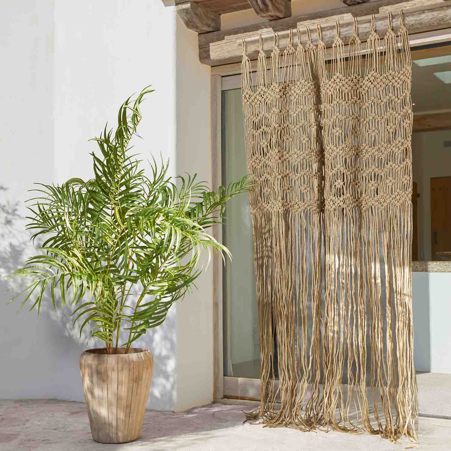 Beige katoenen macramé gordijn met lange franjes bij terrasdeur, plant in pot ernaast