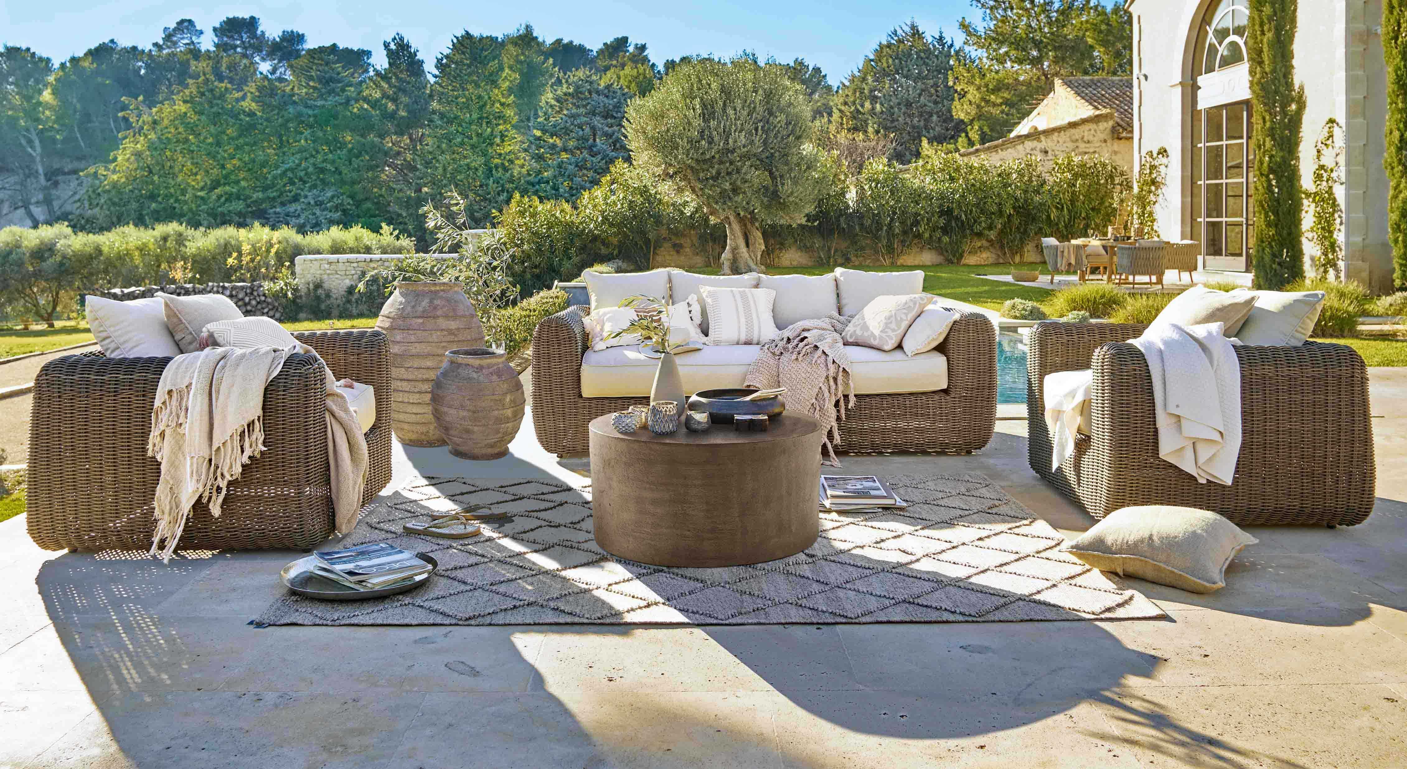 Ensemble de mobilier de jardin en rotin brun avec coussins crème et table basse sur terrasse ensoleillée