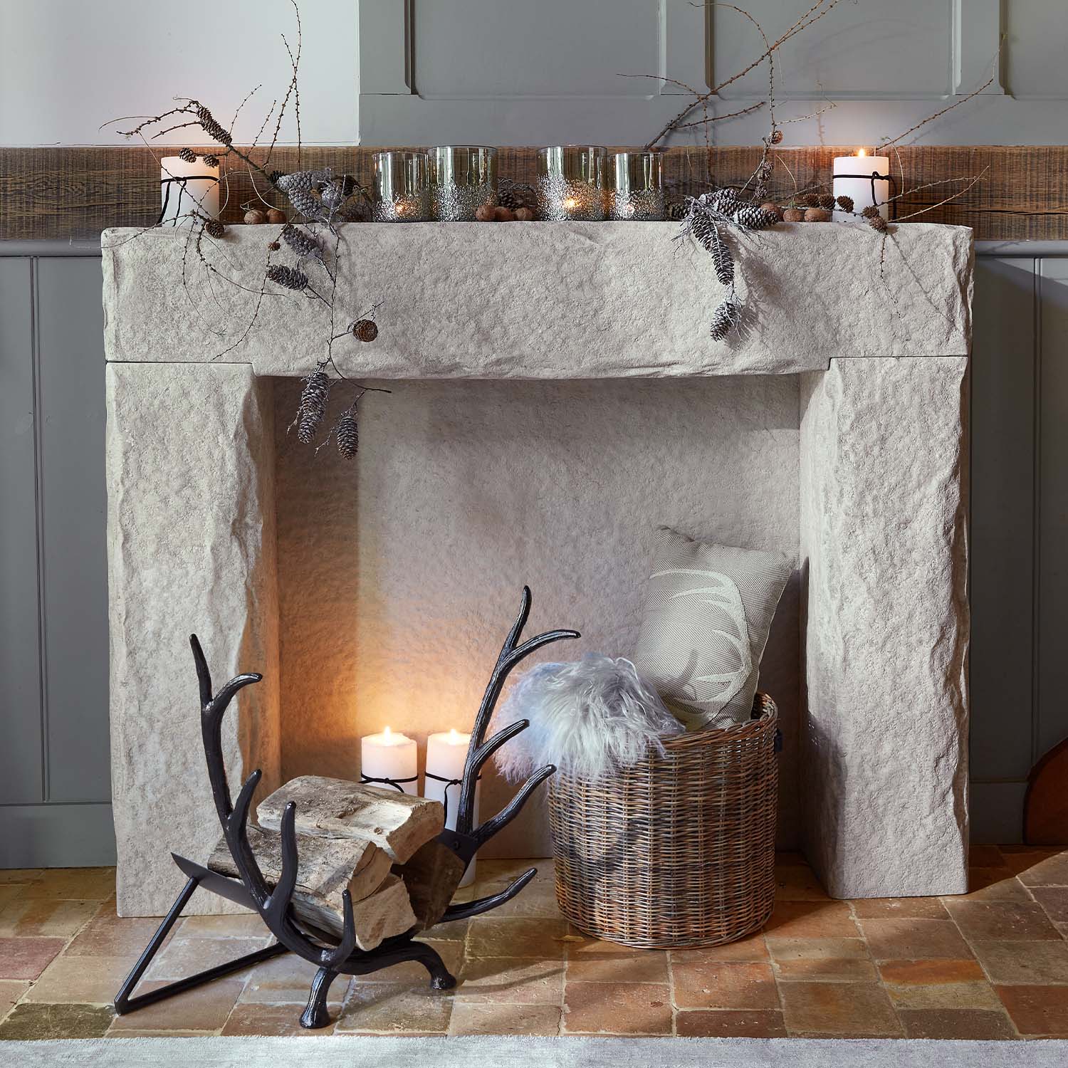 Cheminée en pierre décorée de branches, bougies et panier en osier avec coussin et plaid en fausse fourrure