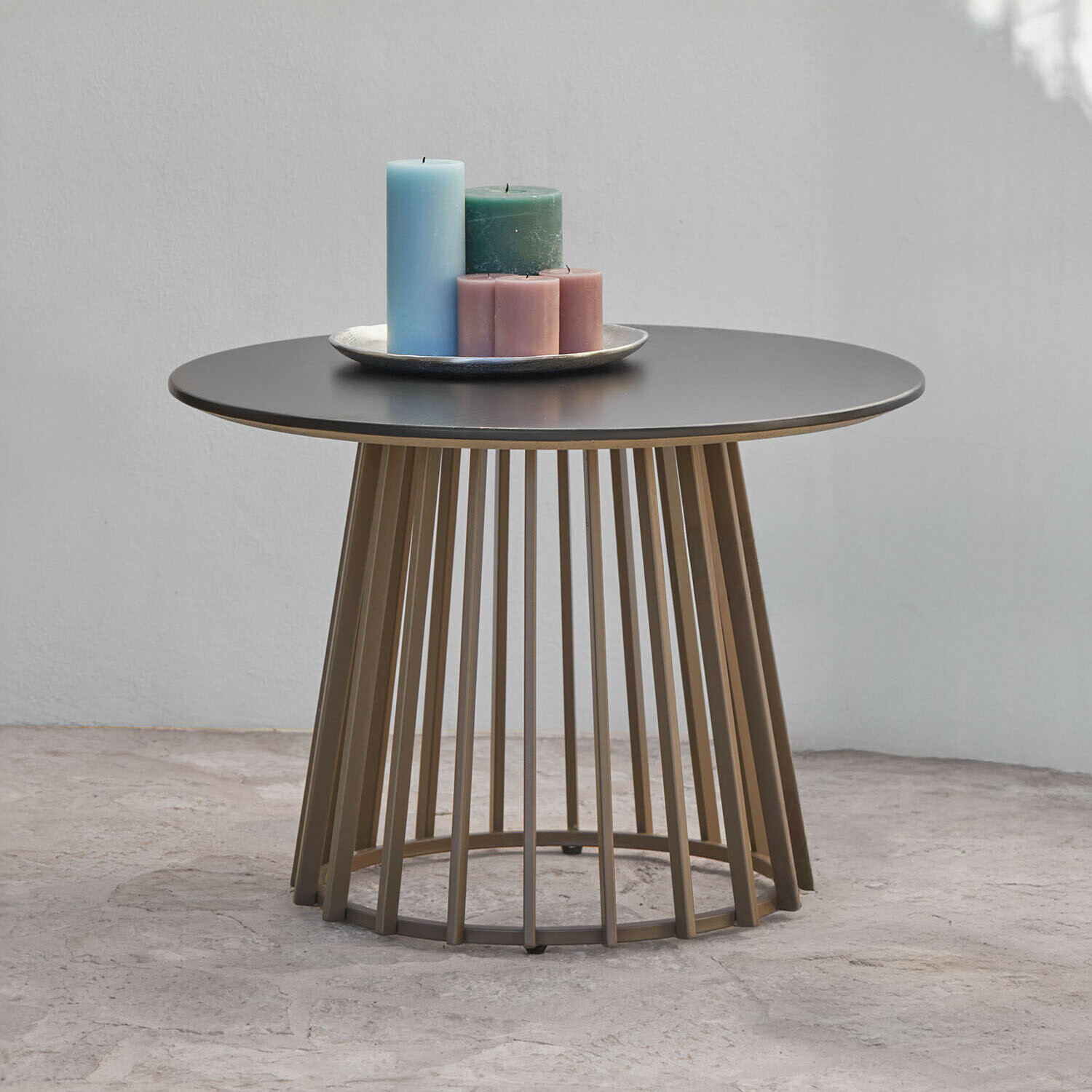 Table basse ronde avec plateau noir en métal et base en barres brunes, décorée de bougies colorées