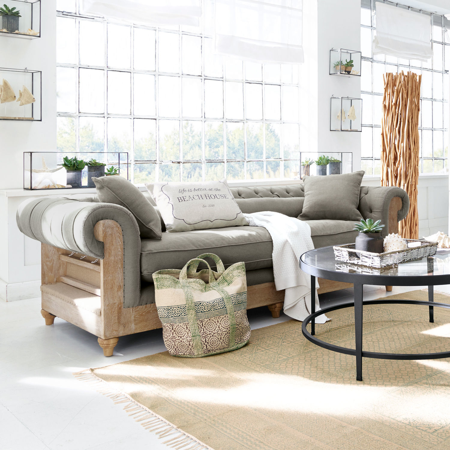 Bank Kanani Grijze bank met houten frame in lichte woonkamer met decoraties en grote ramen