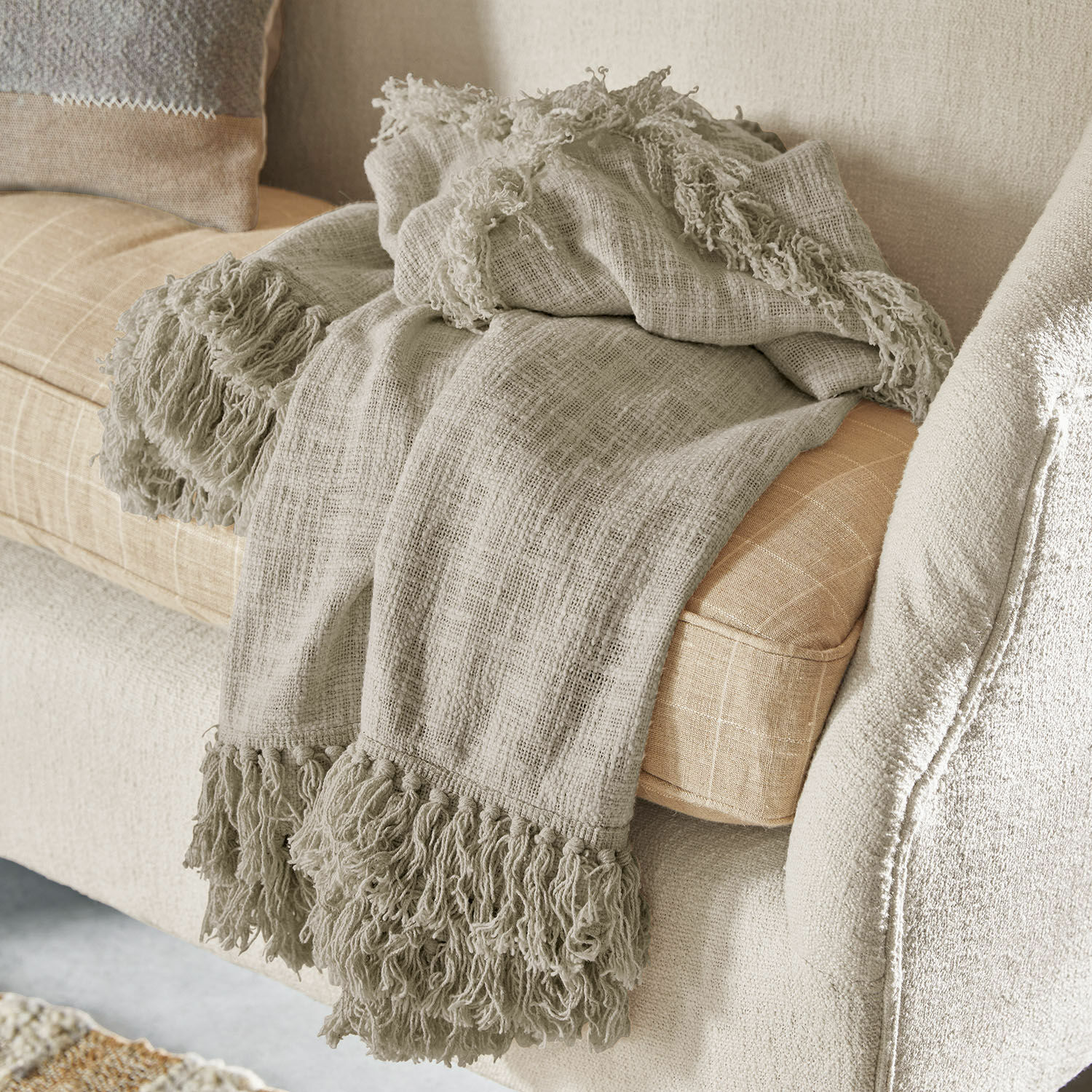 Plaid Freya Plaid beige à franges en tissu doux posé sur un canapé clair, décoration intérieure cosy