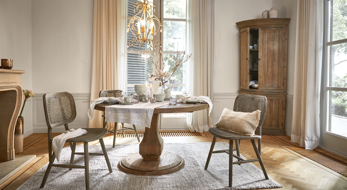 Eetkamer met ronde houten tafel en natuurlijke rotan stoelen, lichte gordijnen