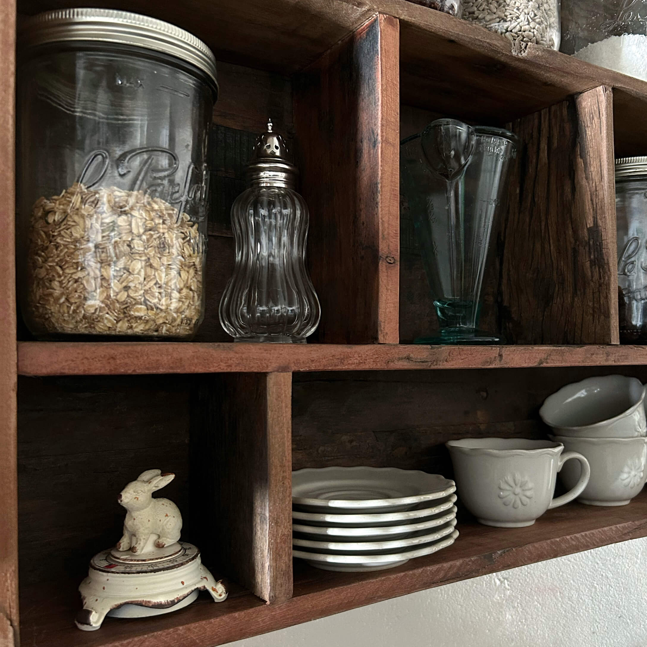 Houten plank met doorzichtige glazen potten en wit keramisch servies in keuken
