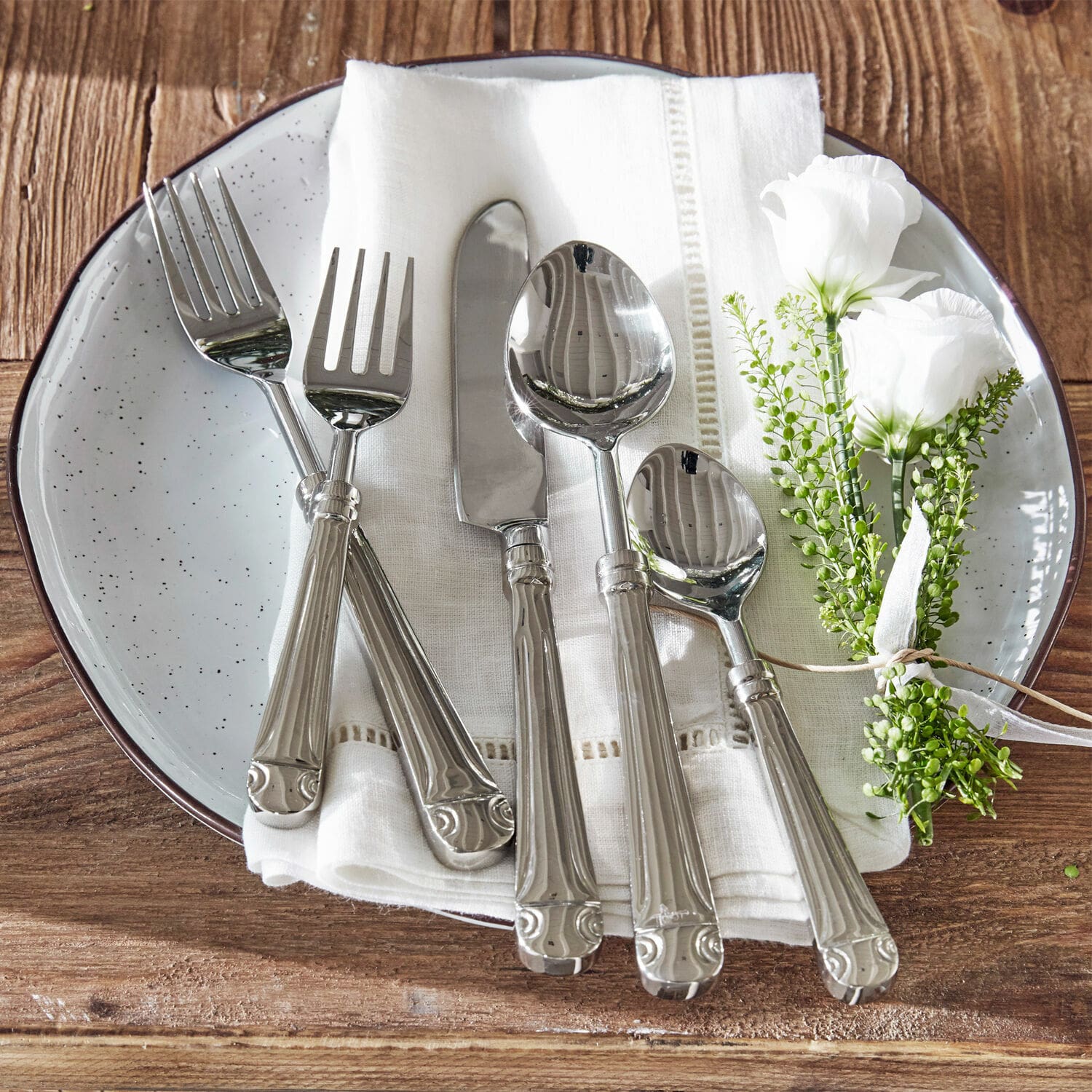 Couverts Eriat Ensemble de couverts en acier inoxydable sur nappe blanche avec décoration florale sur table en bois