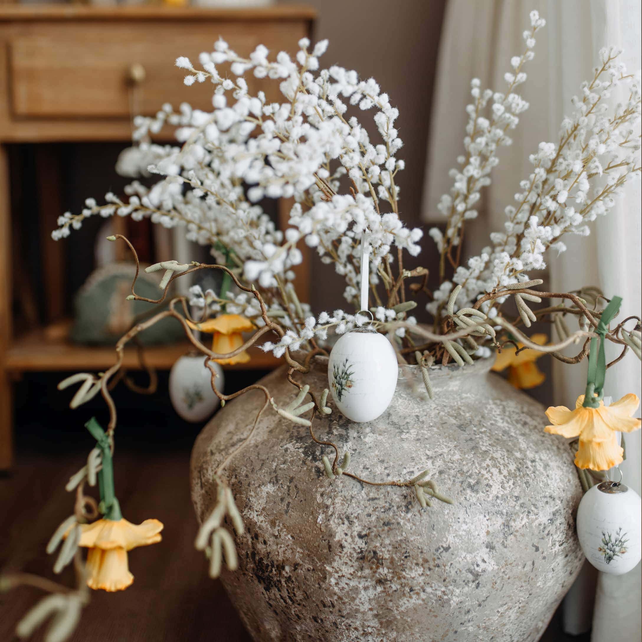 Vase en pierre grise avec branches décoratives et ornements de Pâques aux couleurs pastel