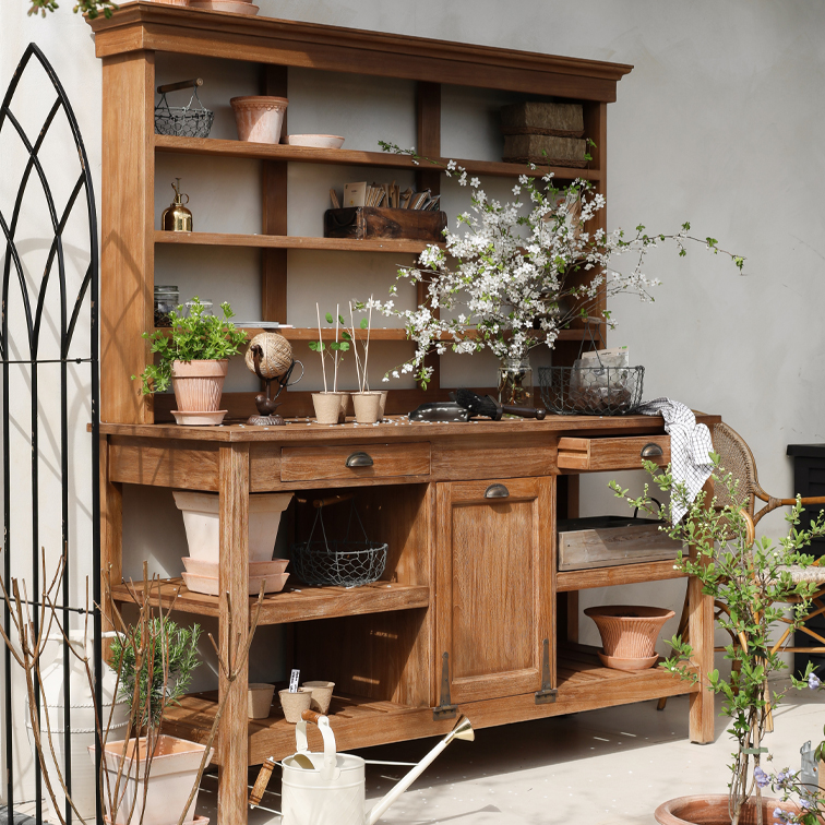 Meuble de jardin en bois avec étagères, pots de fleurs et branches fleuries, ambiance naturelle et outils de jardinage