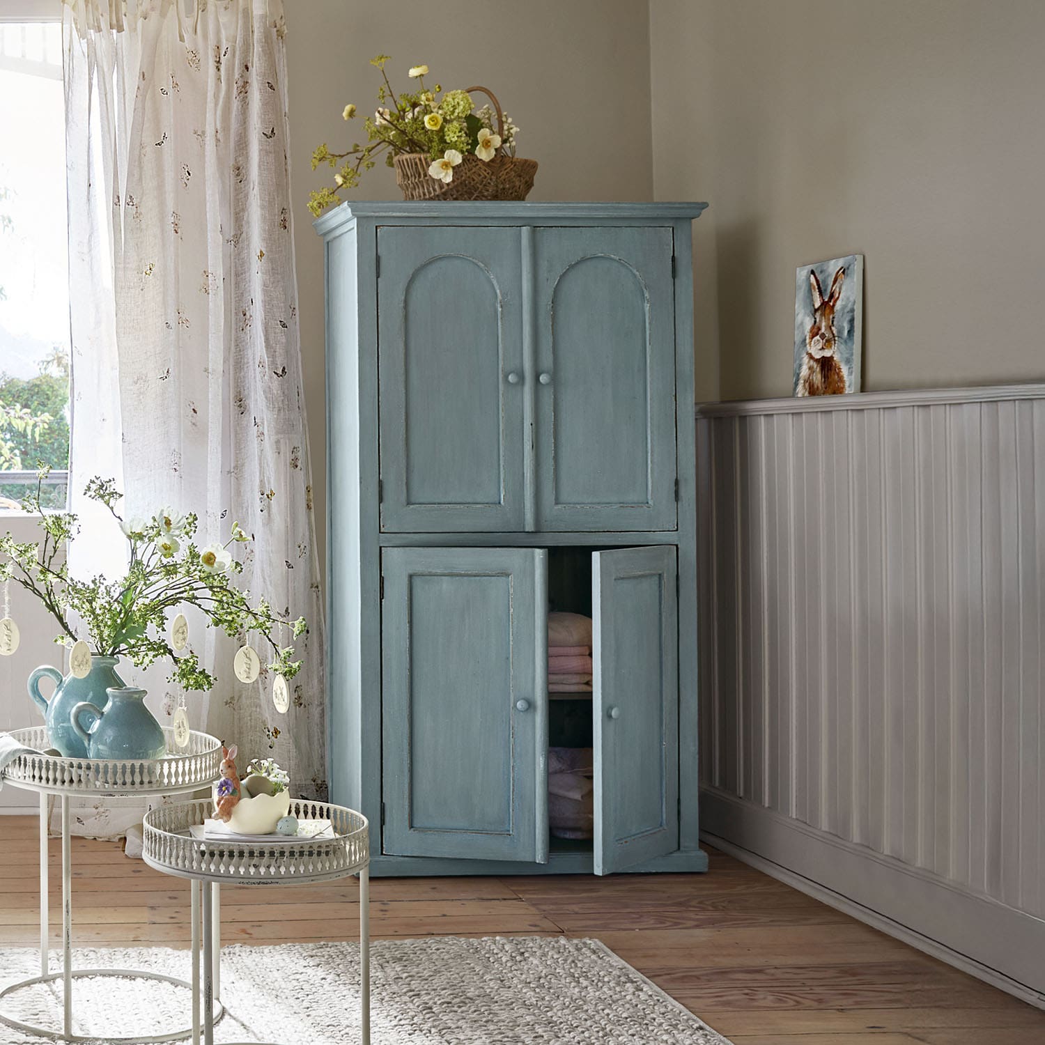Armoire en bois bleu à deux portes dans une pièce lumineuse décorée pour le printemps avec des fleurs et des objets décoratifs