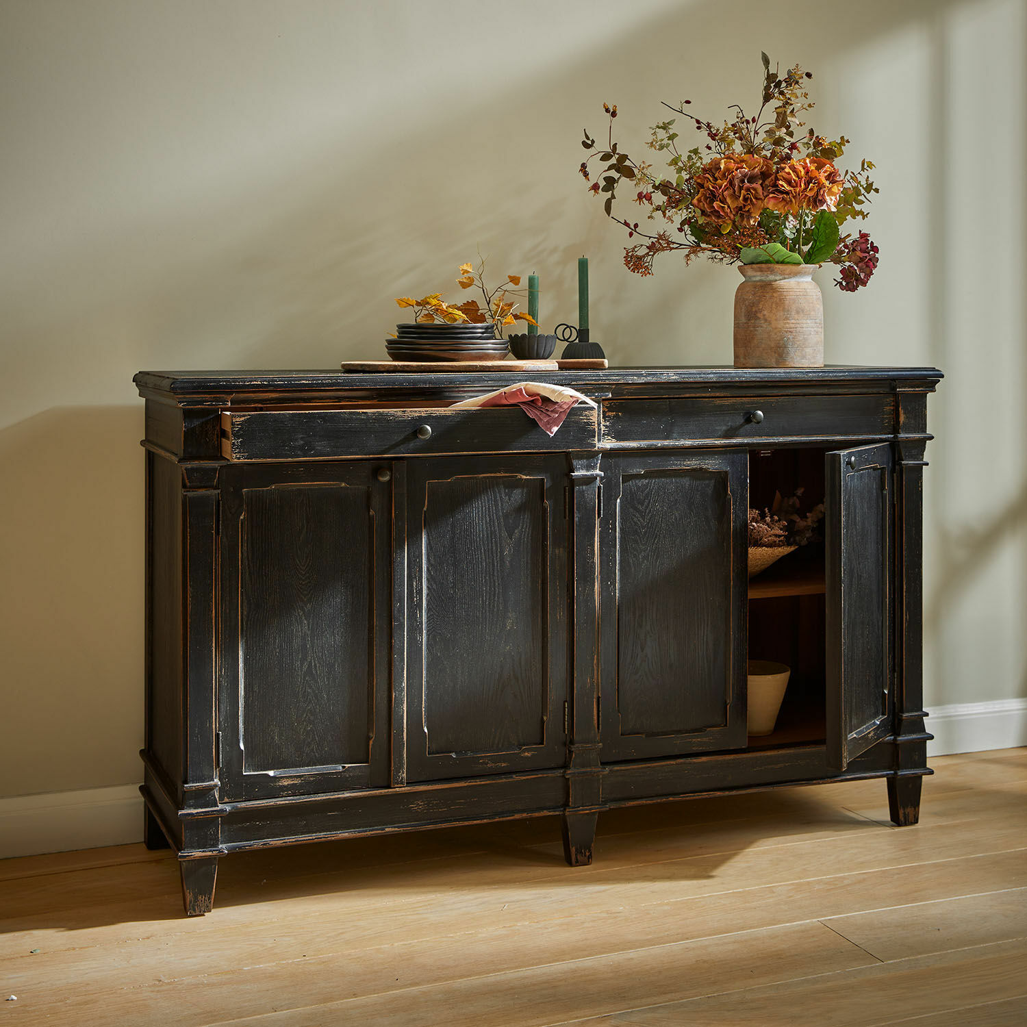 Dressoir Chaveline Zwarte houten dressoir met verouderde afwerking en decoratieve deuren op lichte houten vloer.