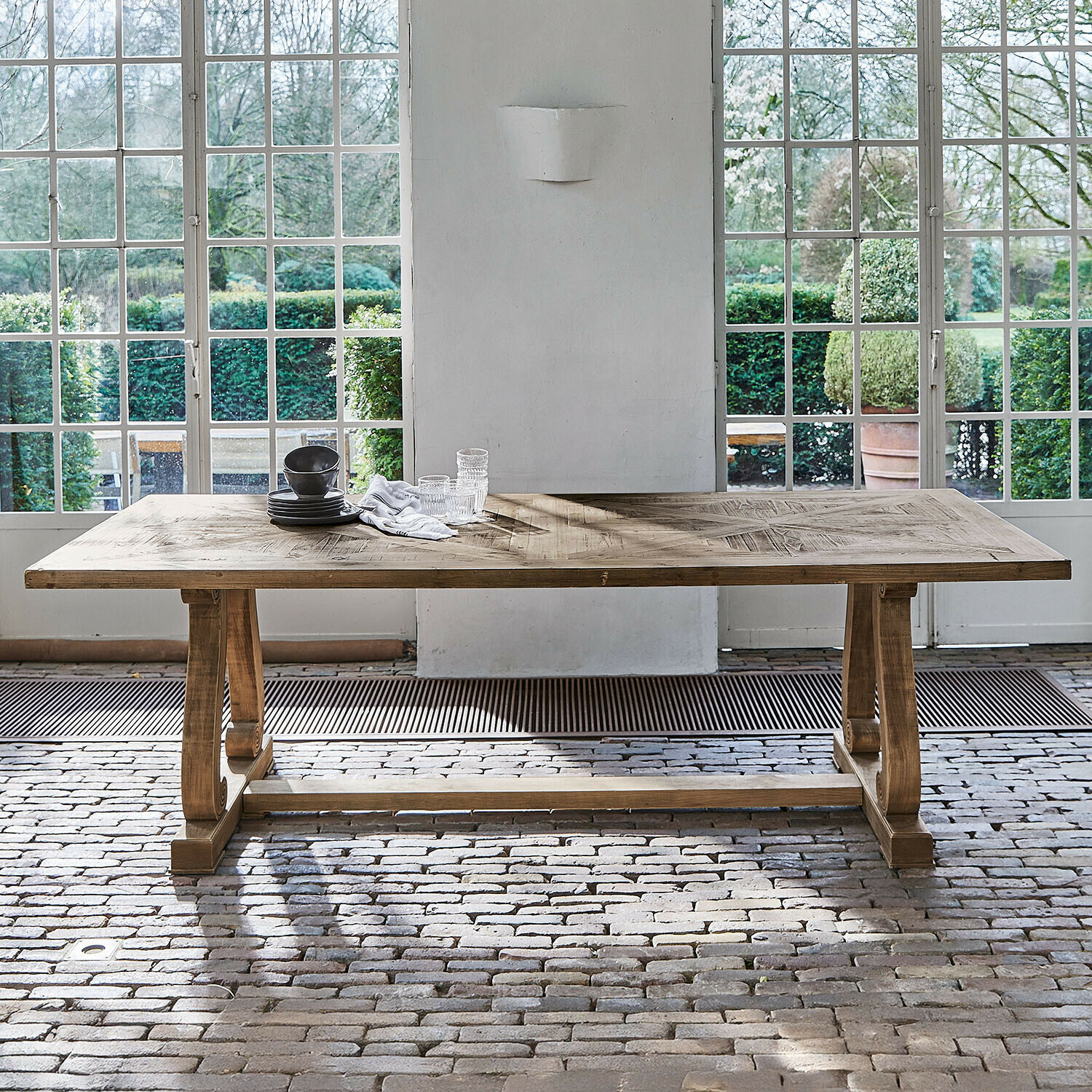 Grande table à manger en bois naturel avec plateau décoratif devant de grandes fenêtres et un sol en briques