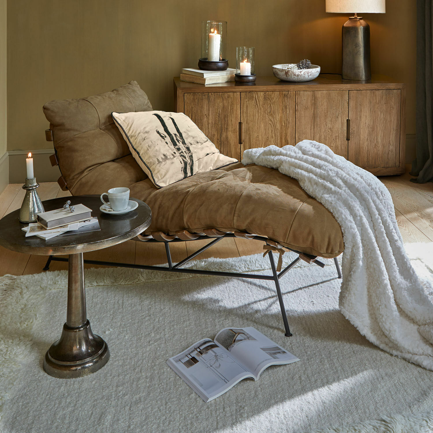 Chaise longue Horraine Bruine leren fauteuil met witte deken en kussen bij houten dressoir en bijzettafel in woonkamer