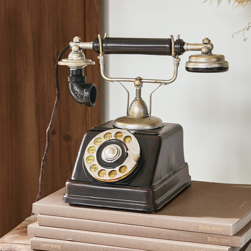 Oude zwarte draaischijftelefoon met metalen onderdelen op een stapel boeken, vintage decoratie