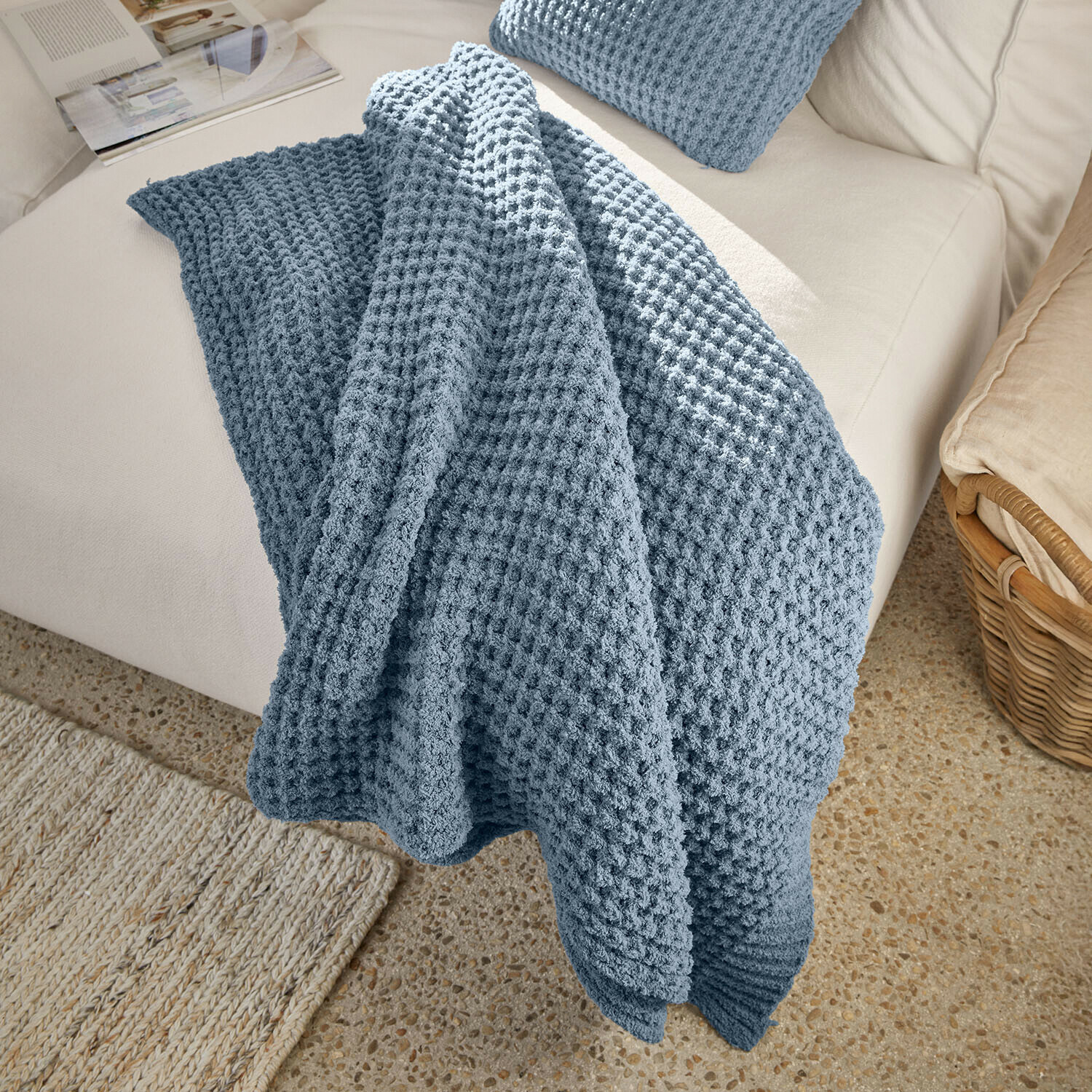 Plaid Ysilda Plaid bleu texturé en nid d'abeille posé sur un canapé clair, couverture décorative et confortable