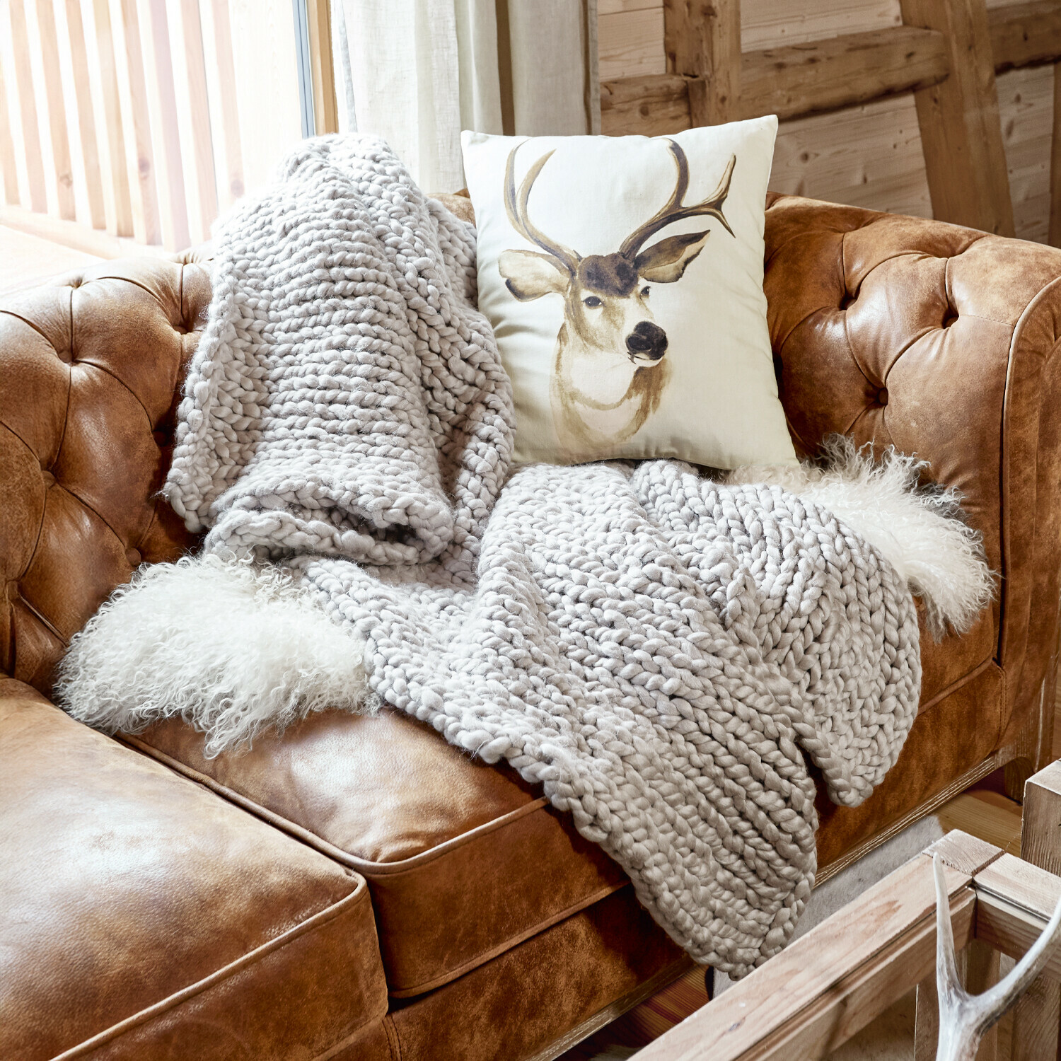 Plaid Reidous Canapé en cuir marron avec couverture épaisse grise et coussin à motif cerf dans un intérieur rustique