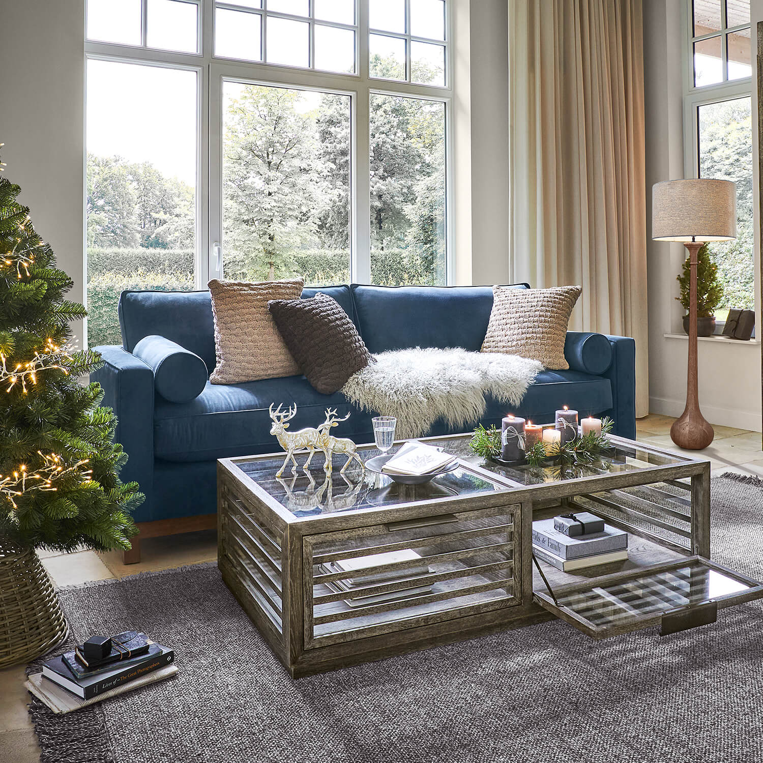 Salon chaleureux avec canapé bleu marine, table basse en verre et décorations de Noël avec sapin et bougies
