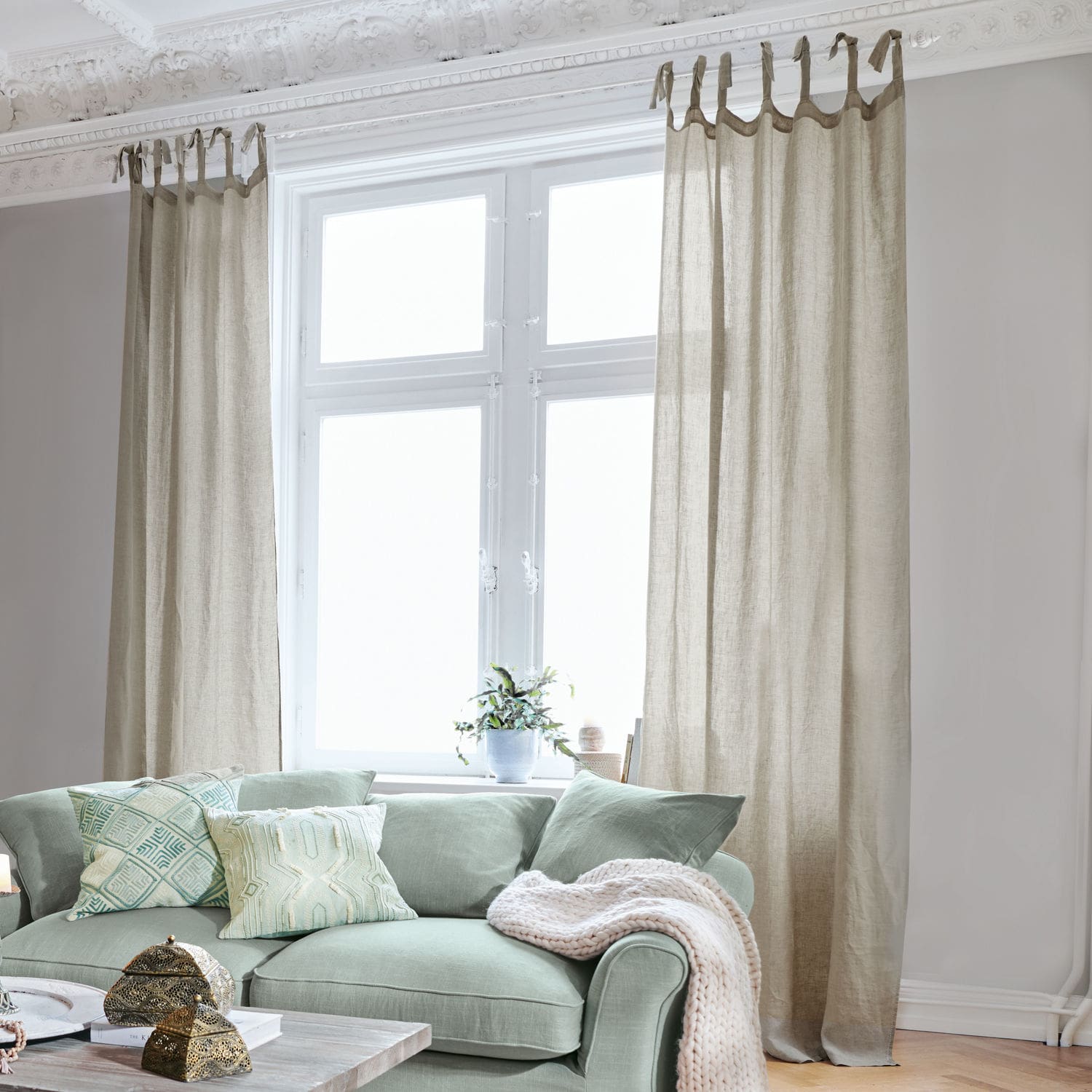 Gordijn Monthelie Beige linnen gordijnen aan raam in lichte woonkamer met groene bank en sierkussens