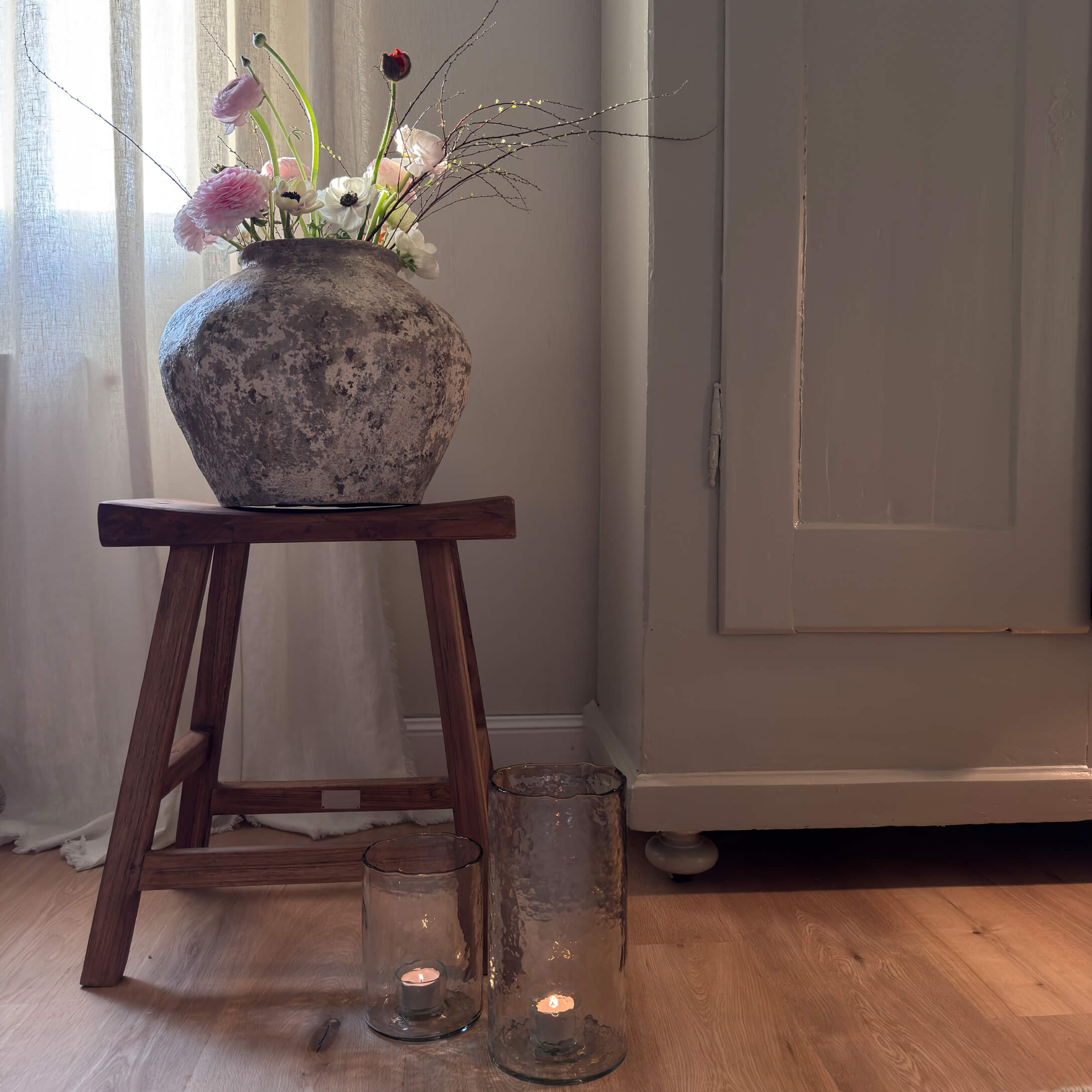 Vase en pierre rustique avec fleurs sur un tabouret en bois à côté de bougies dans des lanternes en verre