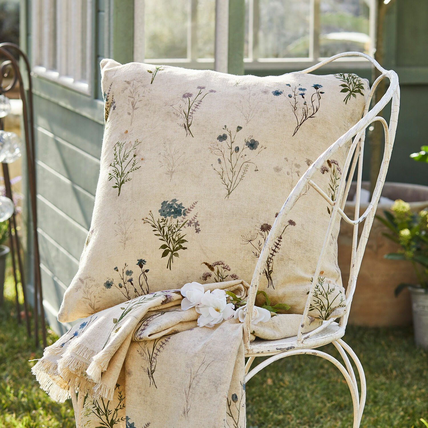 Coussin et plaid en lin beige avec motif floral délicat sur chaise en métal dans un jardin