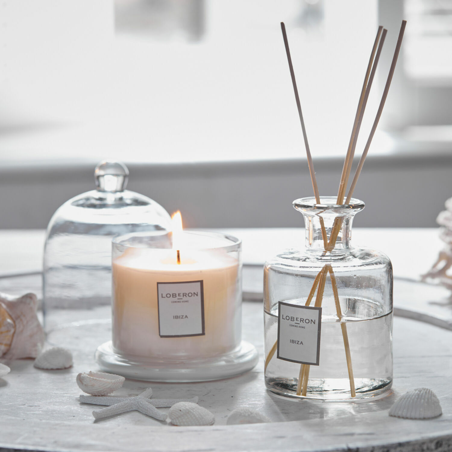 Geurset Vanis Geurkaars en glazen diffuser met stokjes op een wit dienblad met schelpen