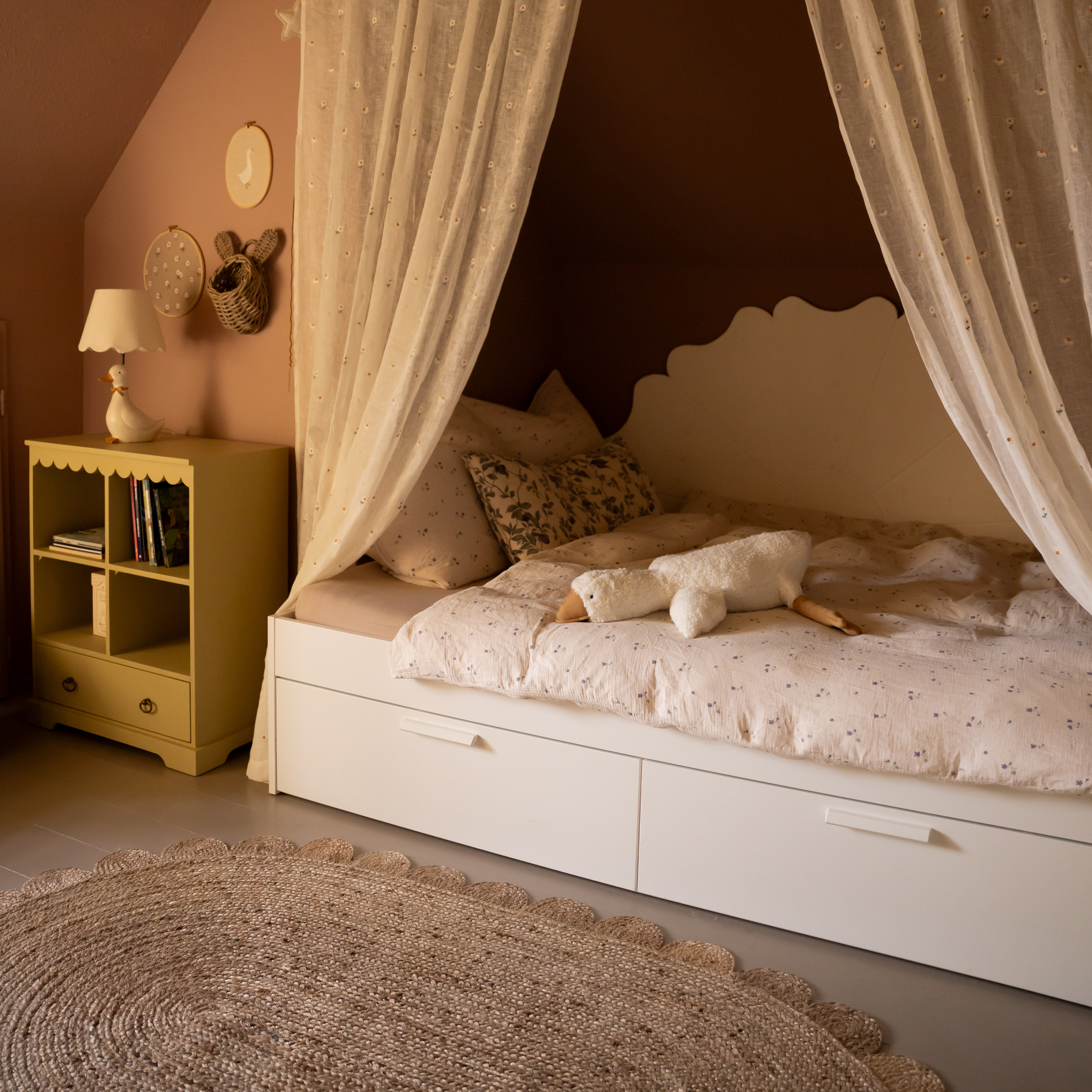 Lit enfant blanc avec rideaux légers et peluche oie sur une couette à motifs floraux
