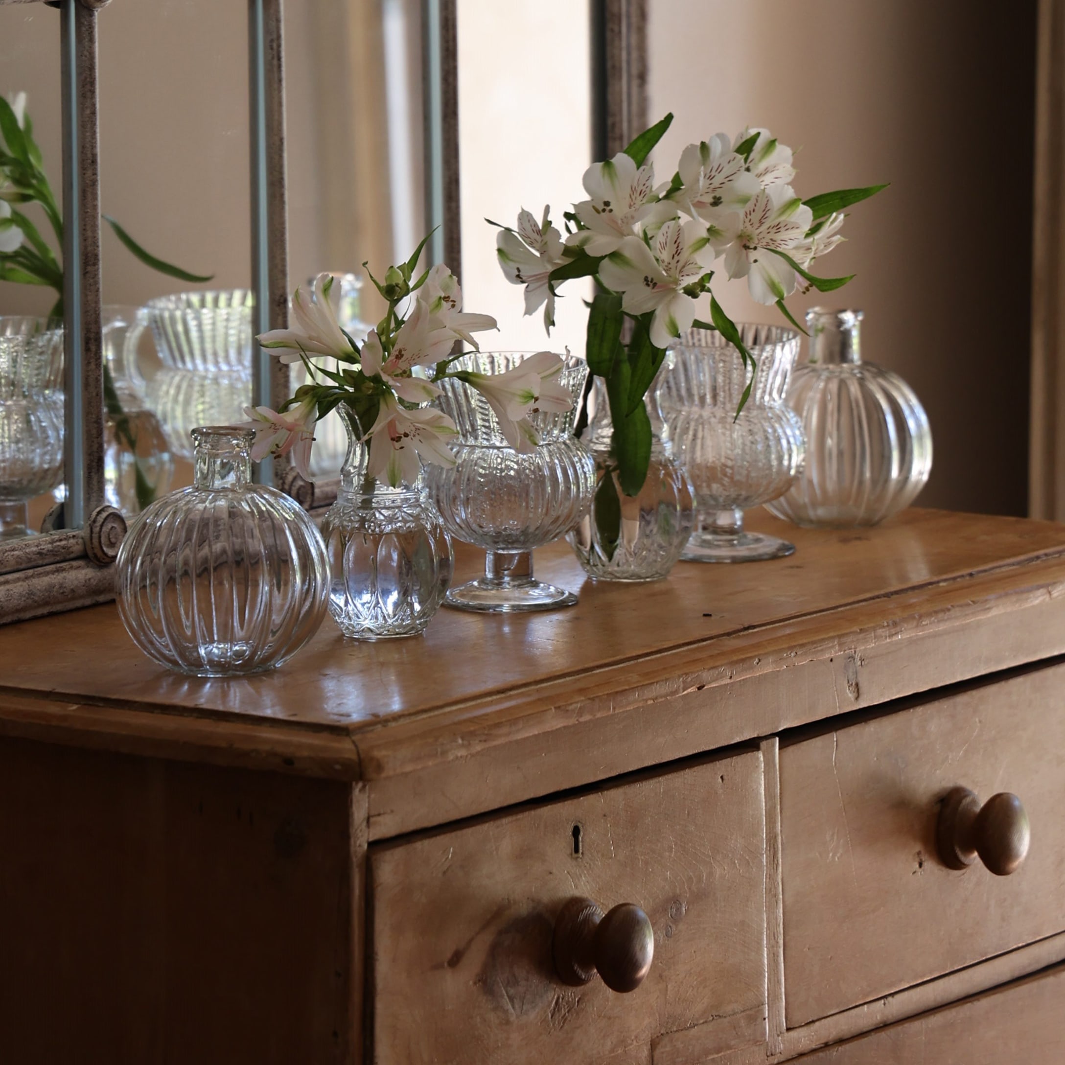 Set transparante glazen vazen met witte bloemen op vintage houten ladekast