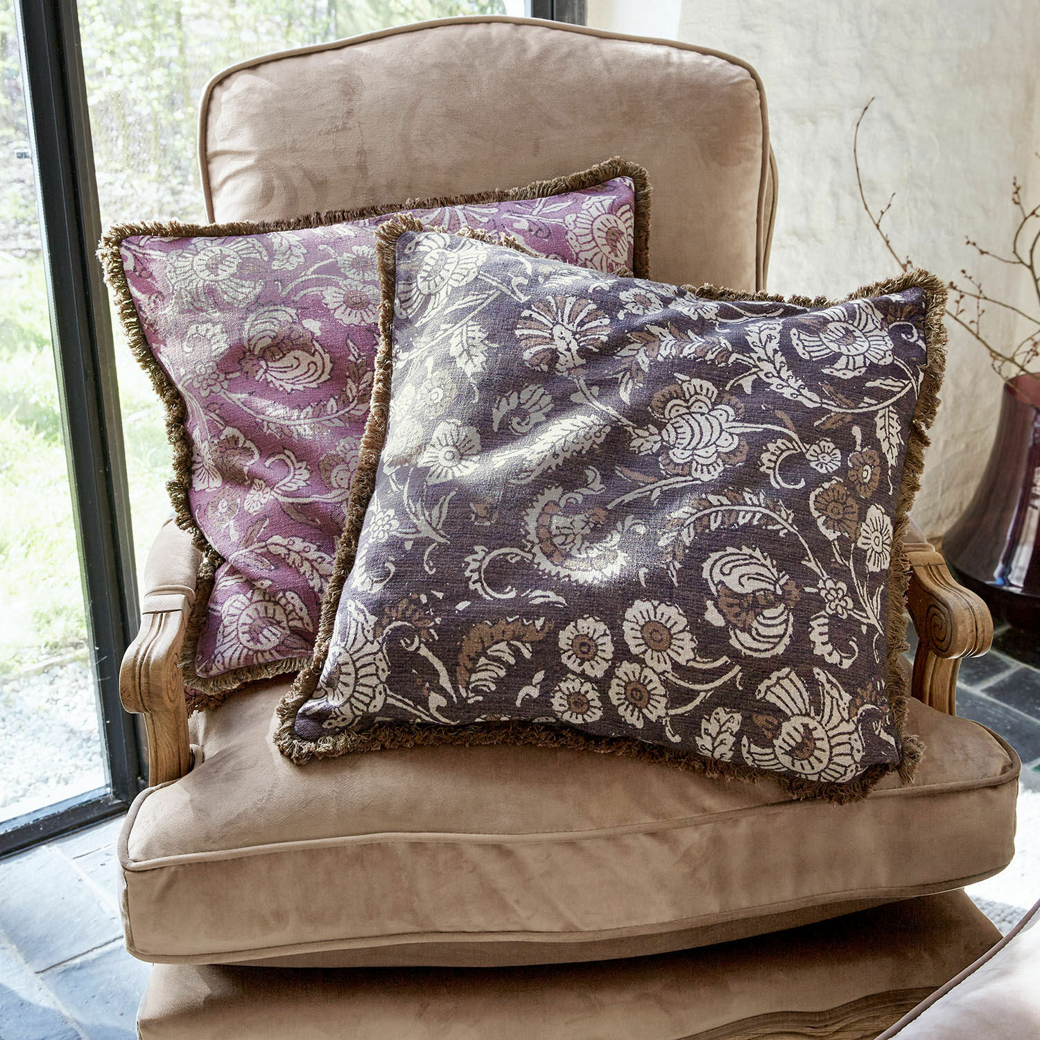 Kussenhoes set van 2 Lalluga Twee decoratieve kussens met bloemenpatroon in paars en grijs op een beige fauteuil
