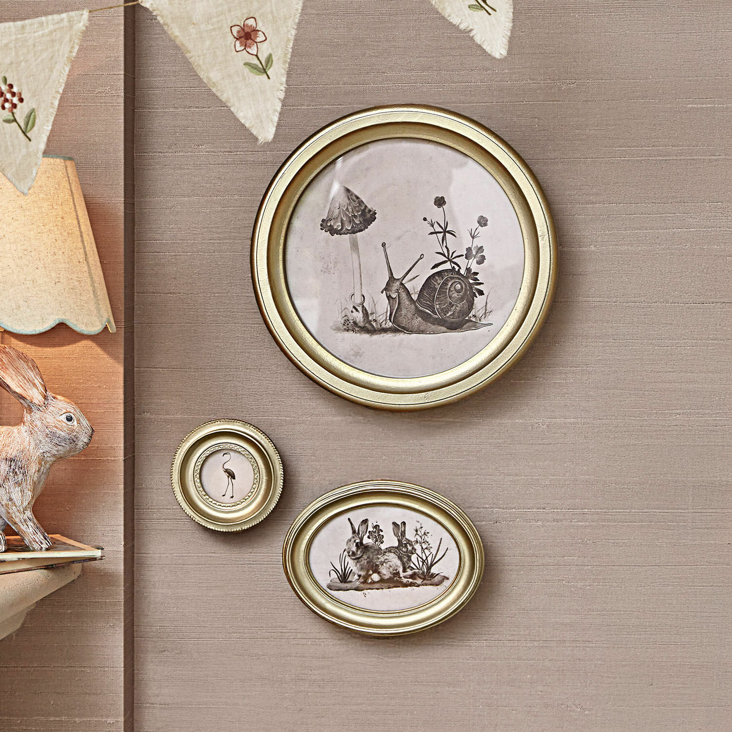 Lot de 3 cadres Atriana Ensemble de trois cadres dorés avec illustrations noir et blanc d'animaux et plantes sur mur beige.