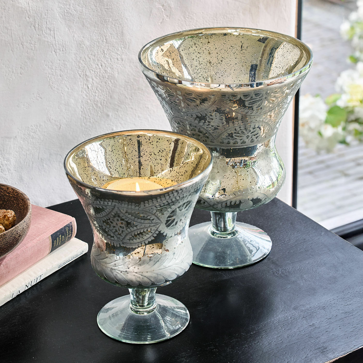 Lot de 2 photophores Zorayne Deux photophores en verre avec motif de feuilles et finition argentée posés sur une table noire