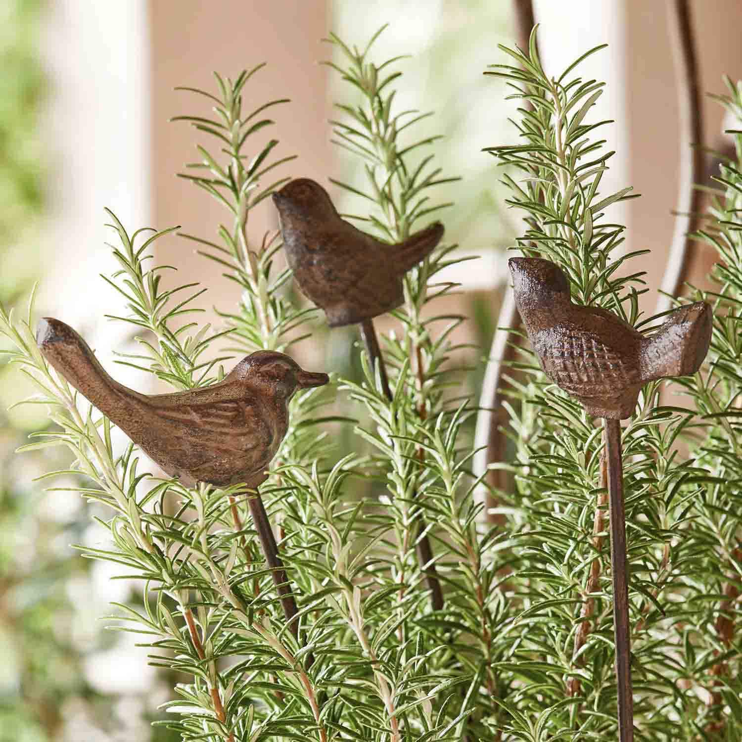 Oiseaux décoratifs en métal brun sur tiges plantés parmi des branches vertes de romarin