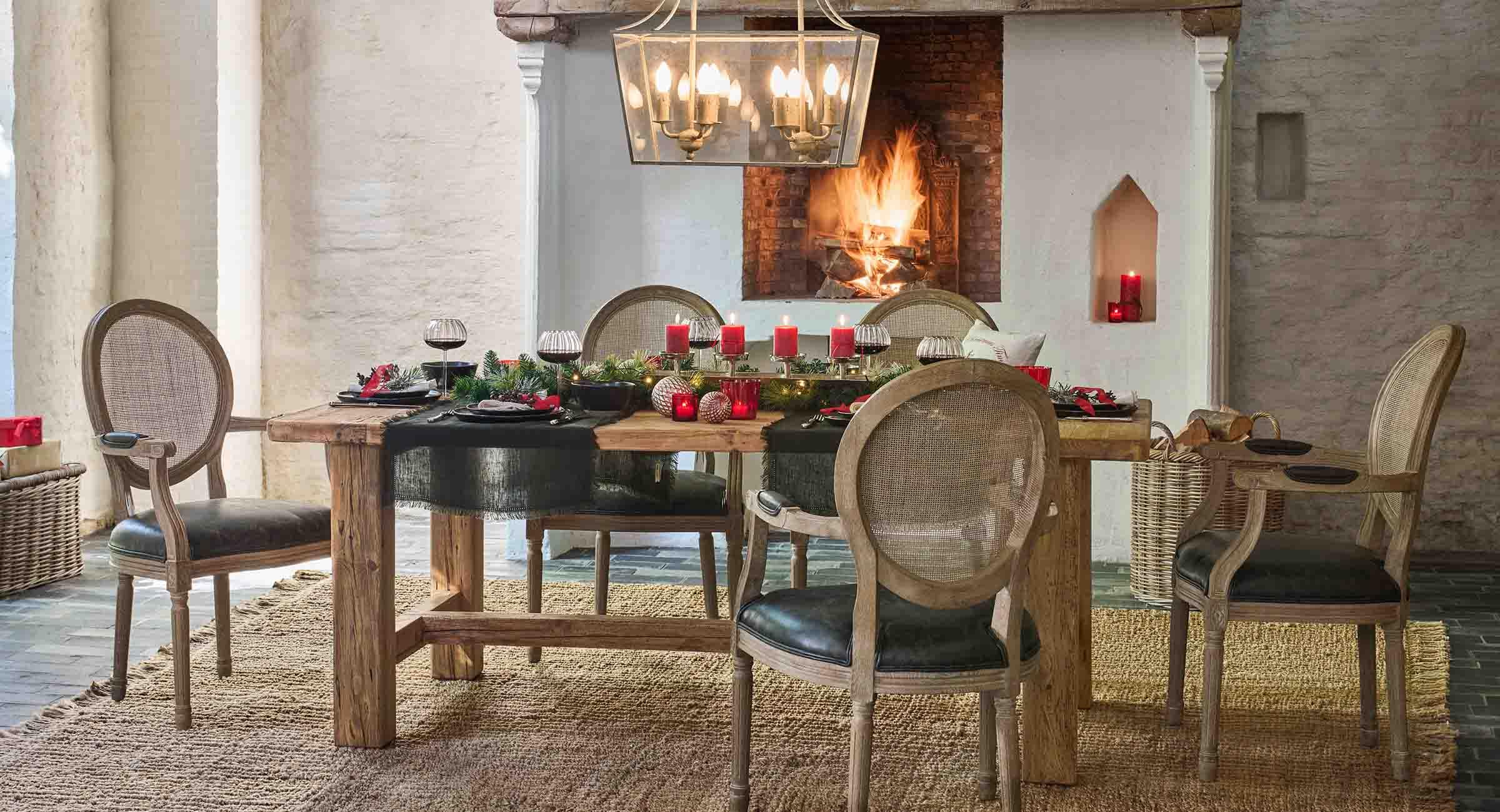 Table en bois rustique décorée de bougies rouges et de verdure naturelle près d'une cheminée allumée