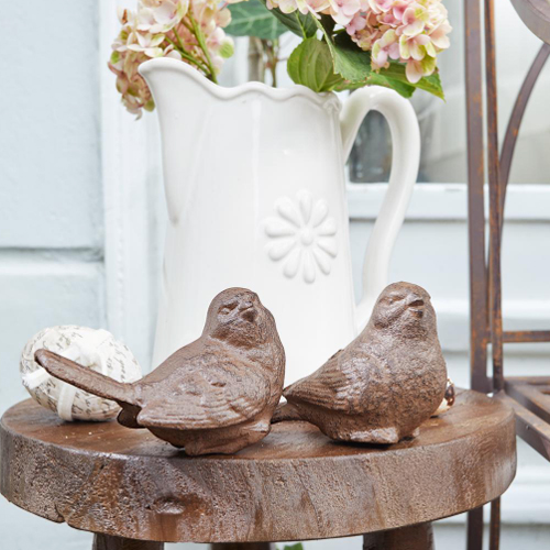 Decoratieve bruine gietijzeren vogels op houten tafel met witte kan op de achtergrond