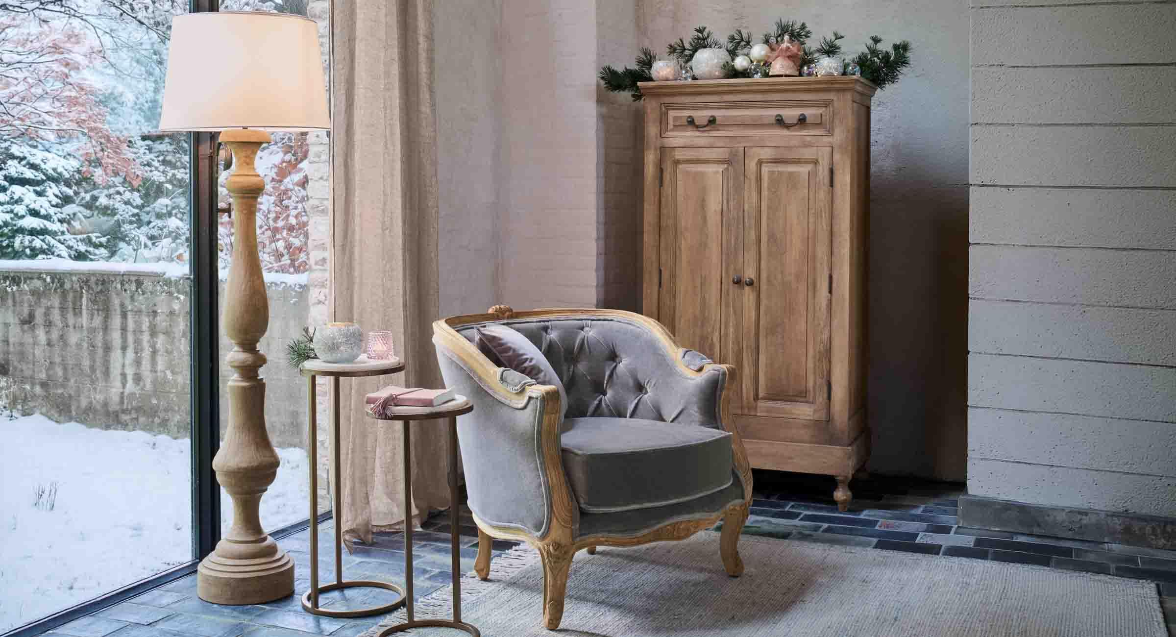 Coin cosy avec fauteuil en velours gris et lampe en bois près d'une fenêtre donnant sur un paysage enneigé