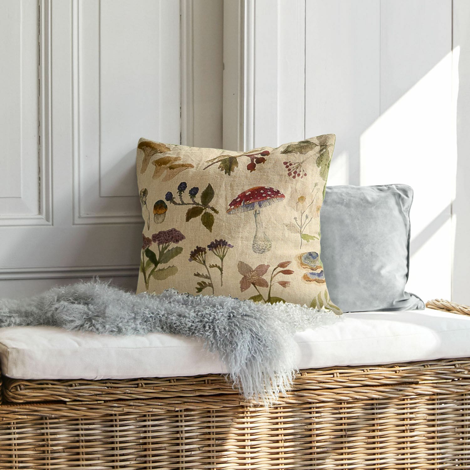 Housse de coussin Selarune Coussin décoratif en lin avec motif végétal naturel posé sur un banc en osier clair